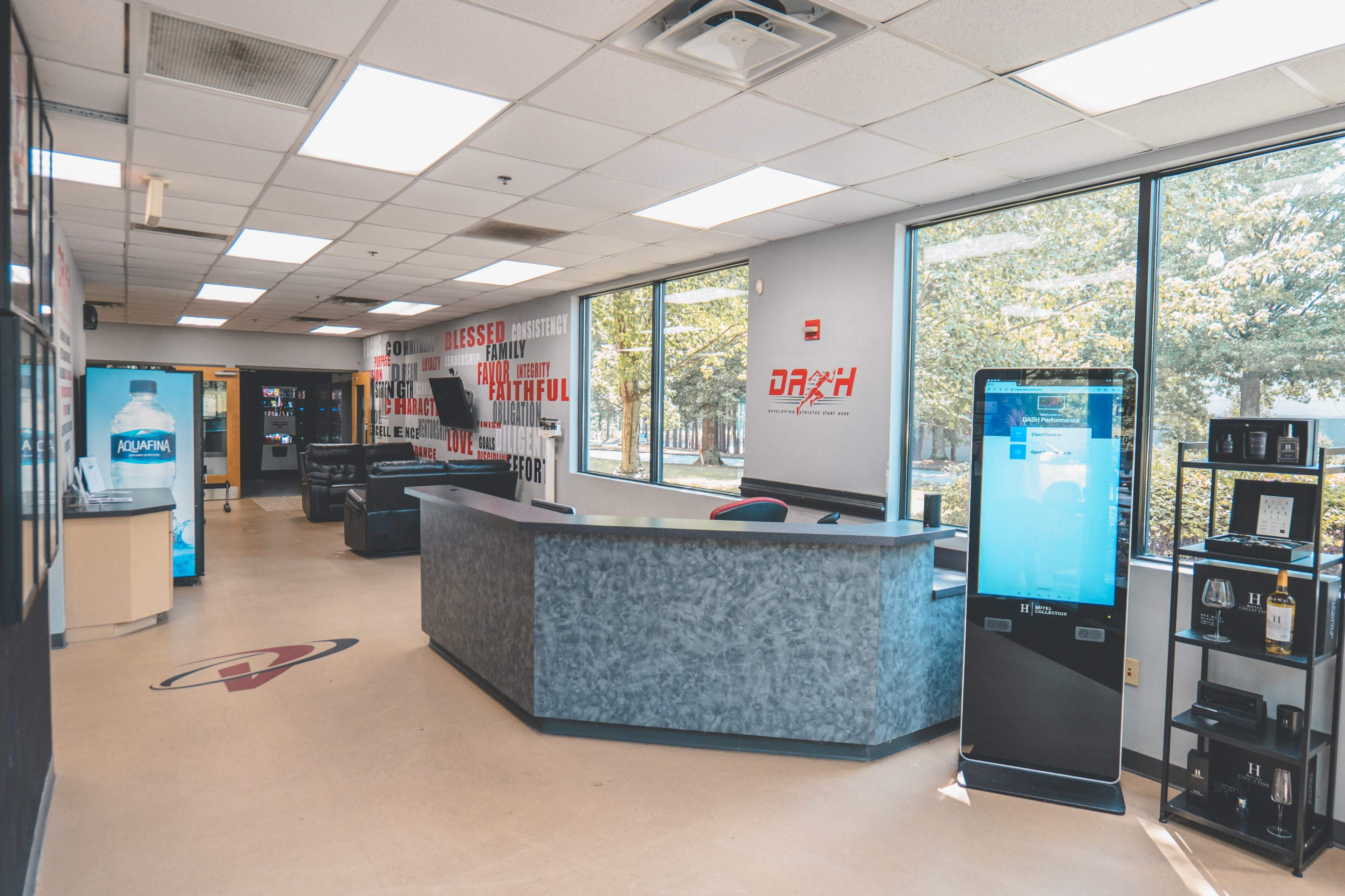 A modern office reception area with a front desk, vending machines, and large windows overlooking a green outdoor space.