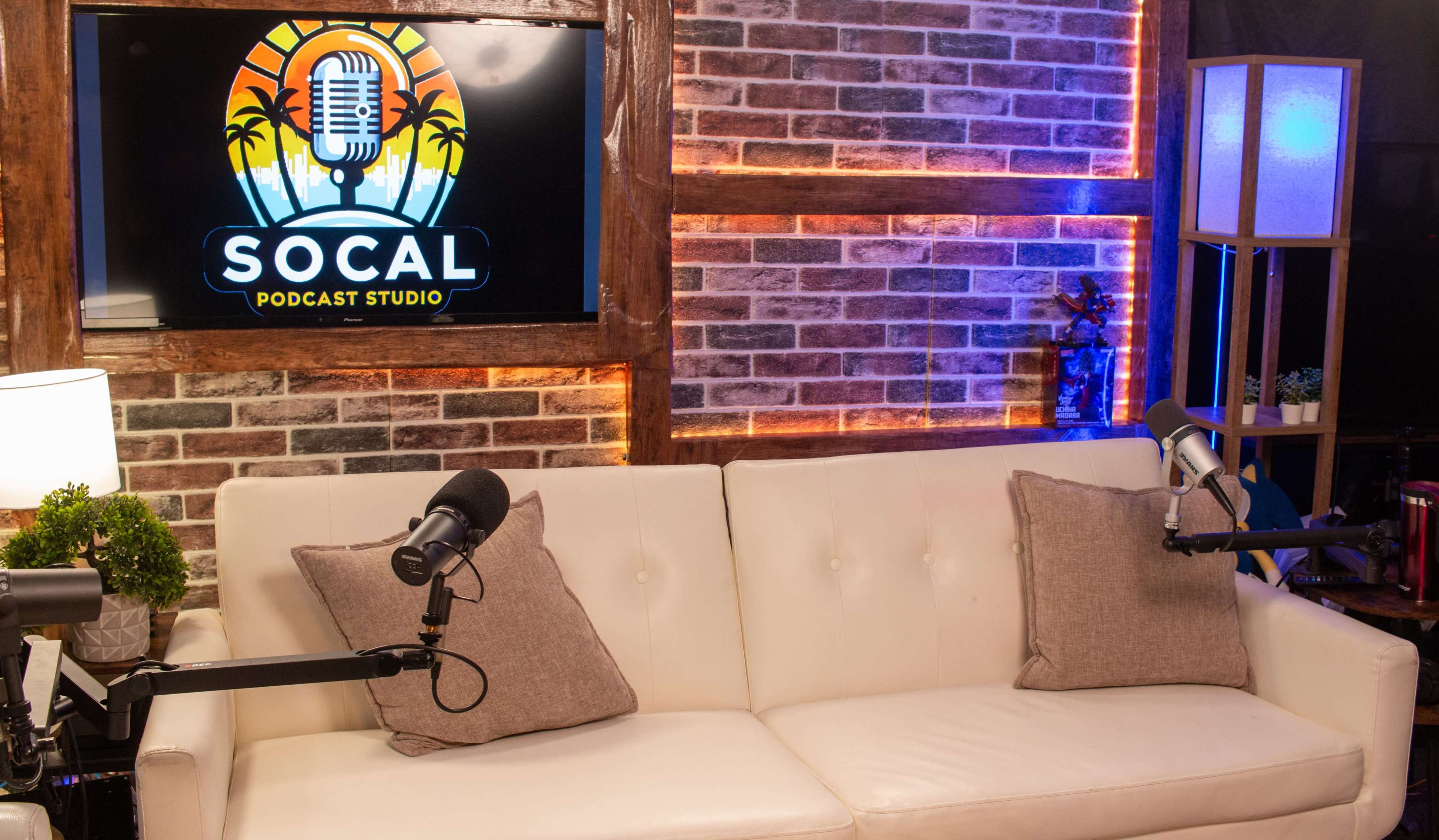 The image shows a podcast studio with a white couch, two microphones, and a wall displaying the "SoCal Podcast Studio" logo with palm trees.