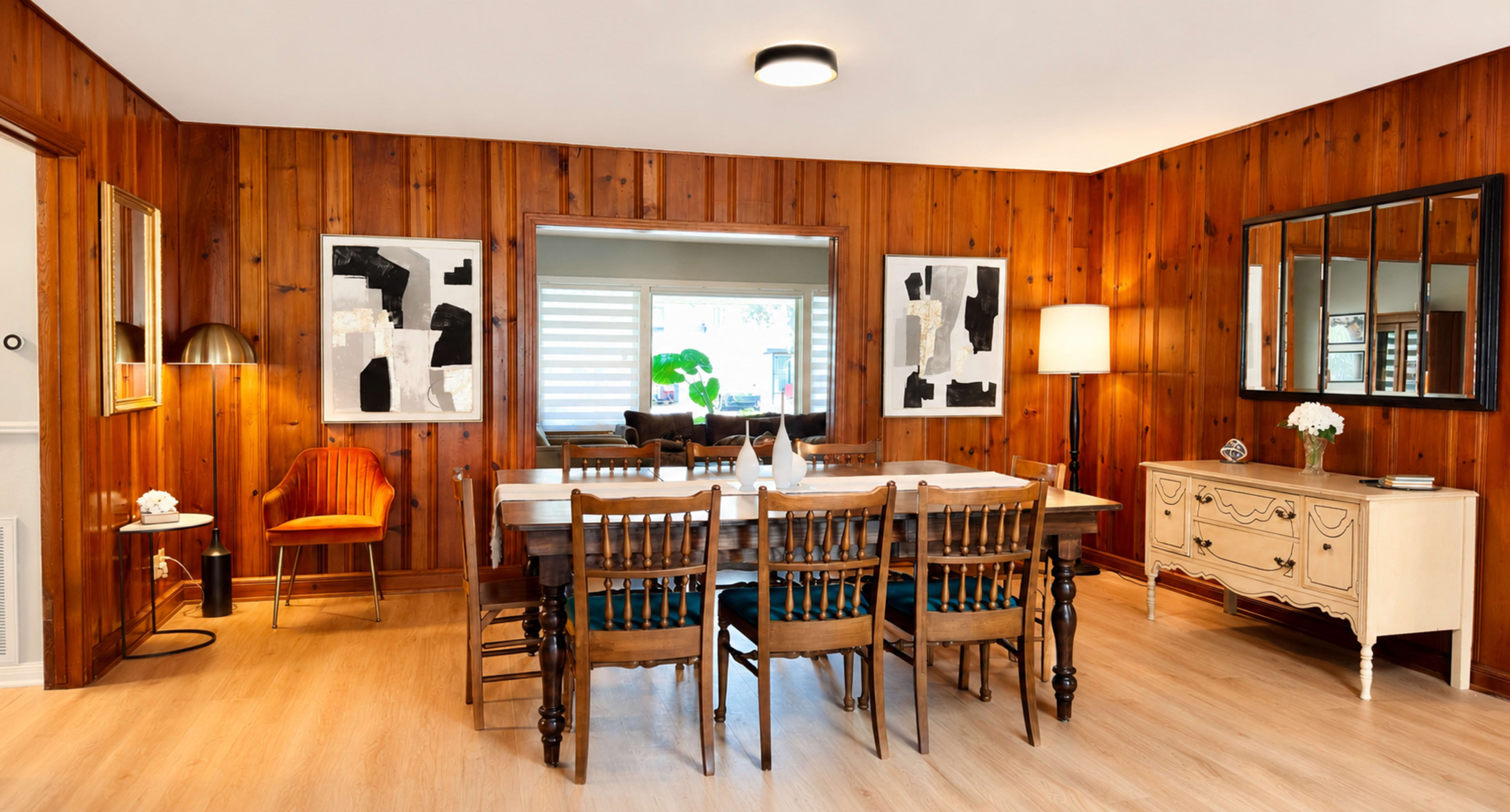 The image shows a dining area with wooden paneling, a large table surrounded by chairs, and art pieces on the walls.