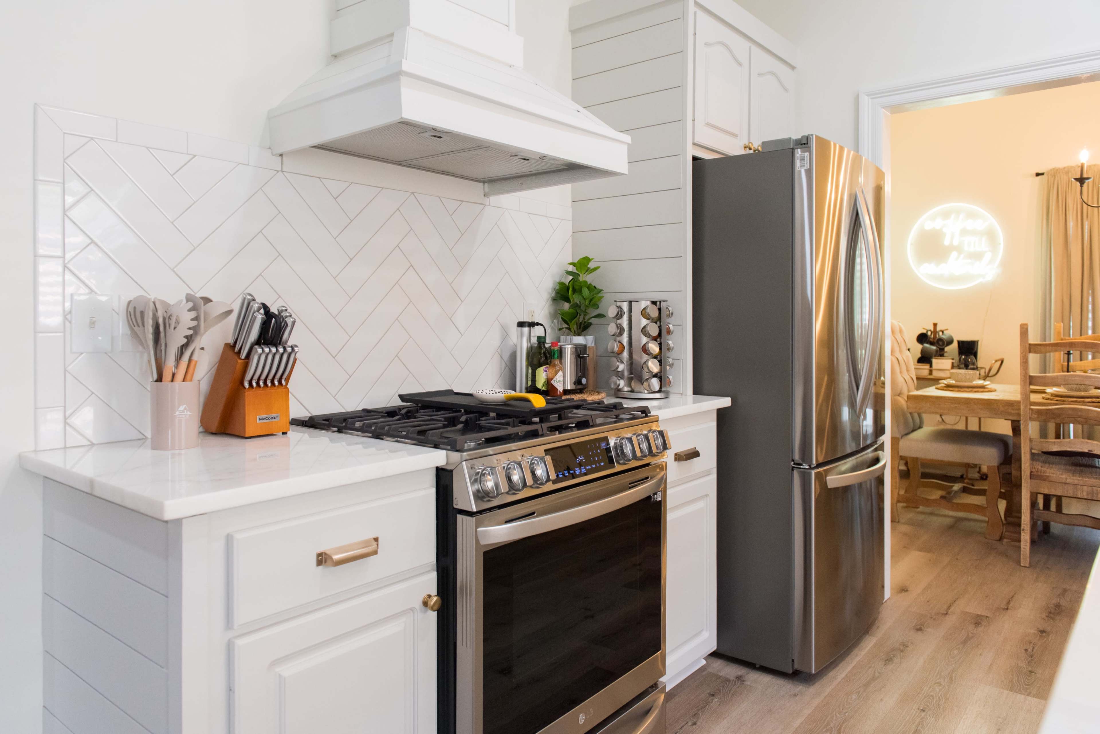 A modern kitchen features a stainless steel stove and refrigerator, herringbone backsplash, and a setup of utensils and spices.