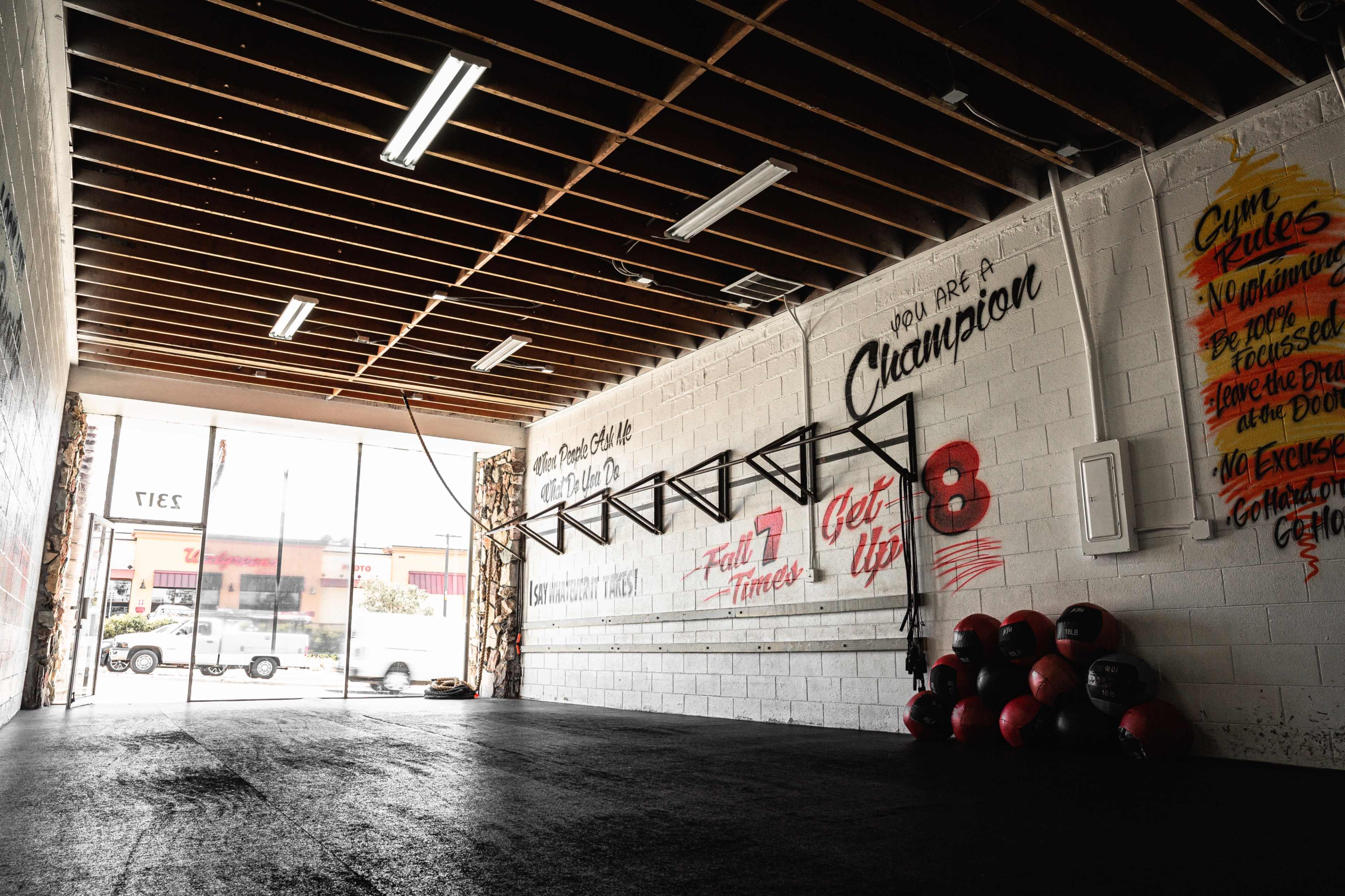 A spacious gym interior featuring exposed beams, wall-mounted workout equipment, and motivational phrases painted on the walls.