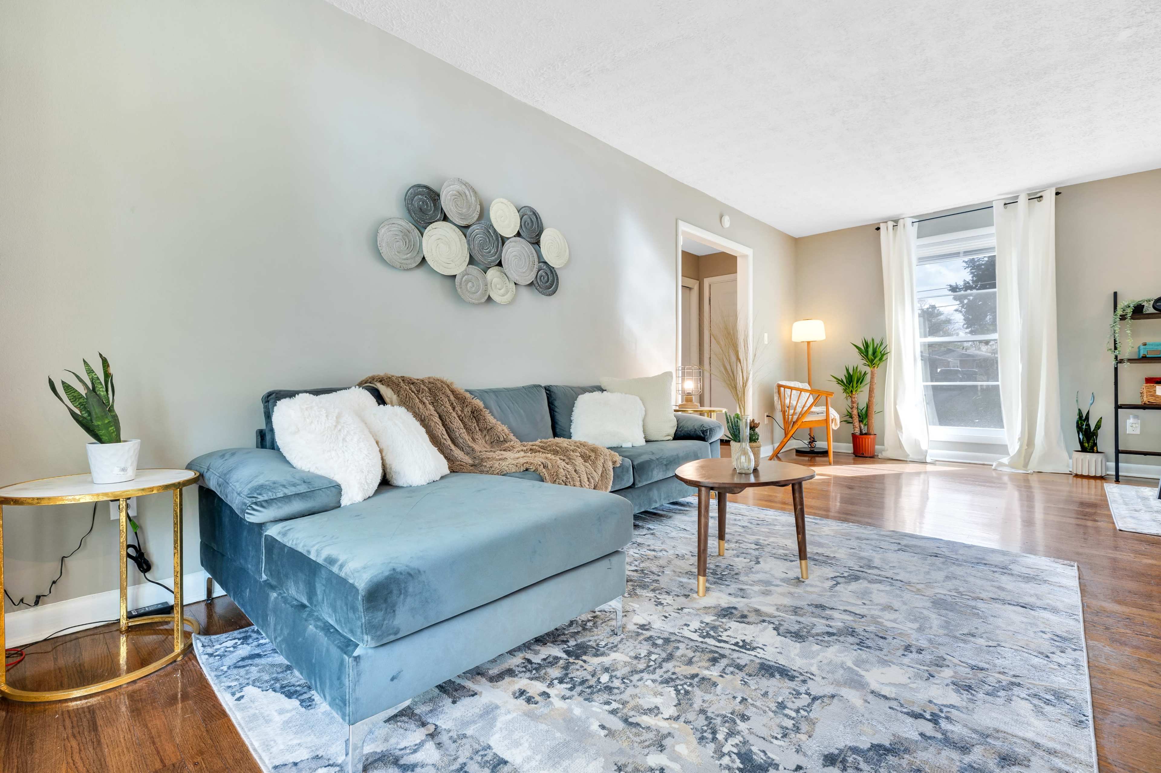 A light-filled living room featuring a blue sectional couch, a round wooden coffee table, and a decorative wall display made of circular items.