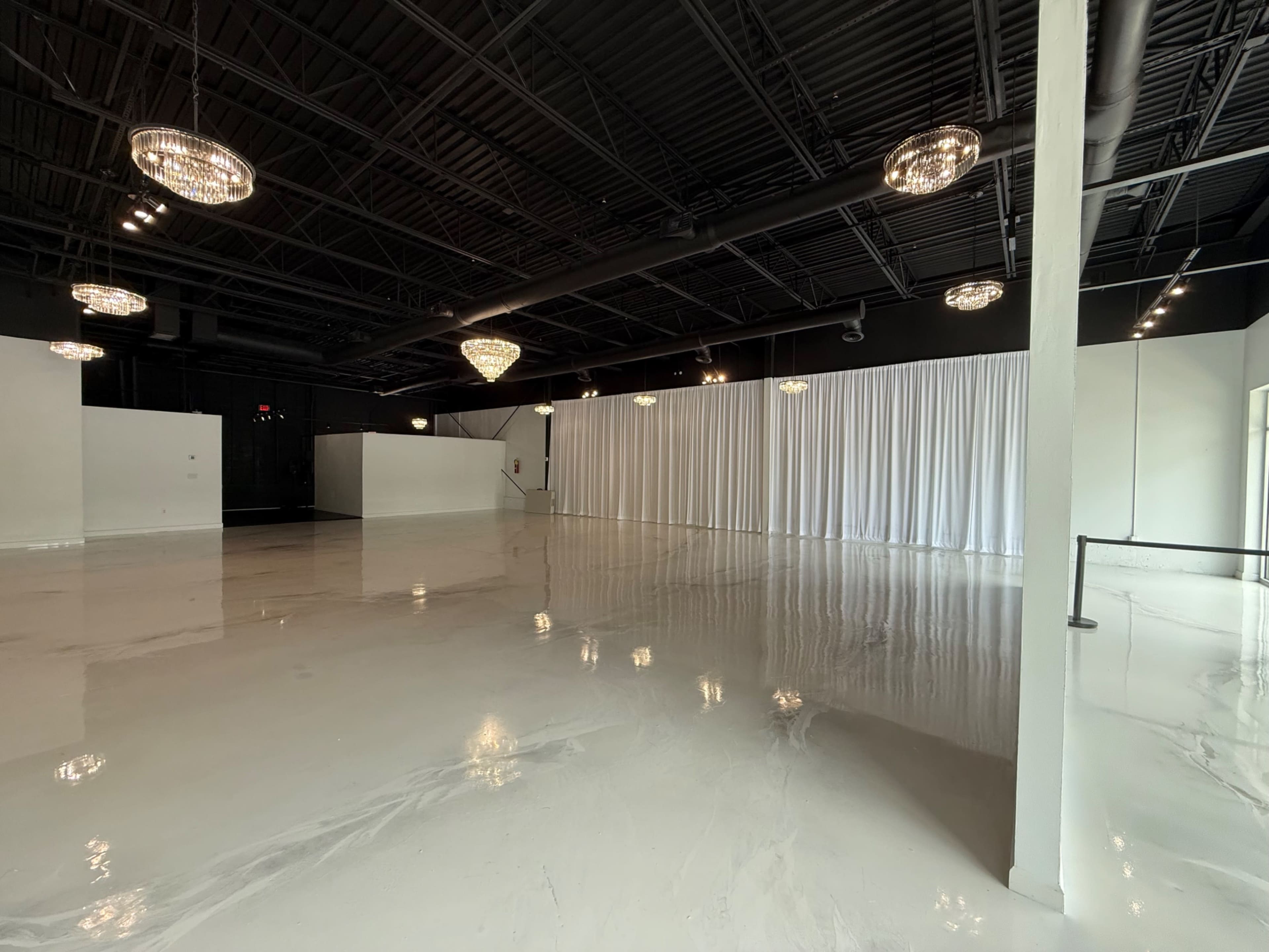 The image shows a spacious, modern interior with polished concrete floors, white curtains, and multiple overhead light fixtures.
