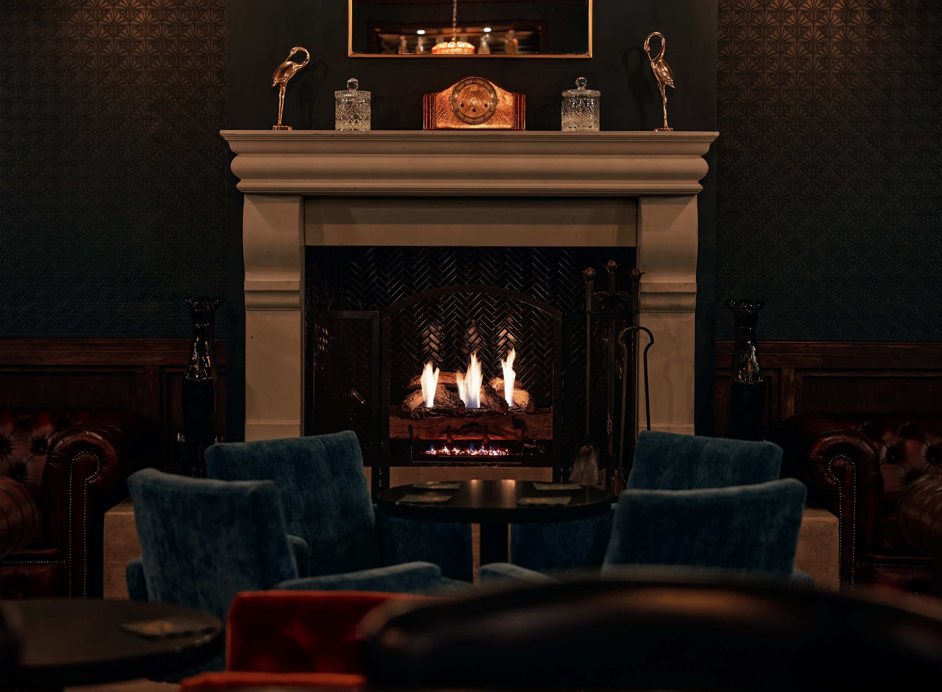 A cozy living room features a fireplace surrounded by blue armchairs and decorative items on the mantle.