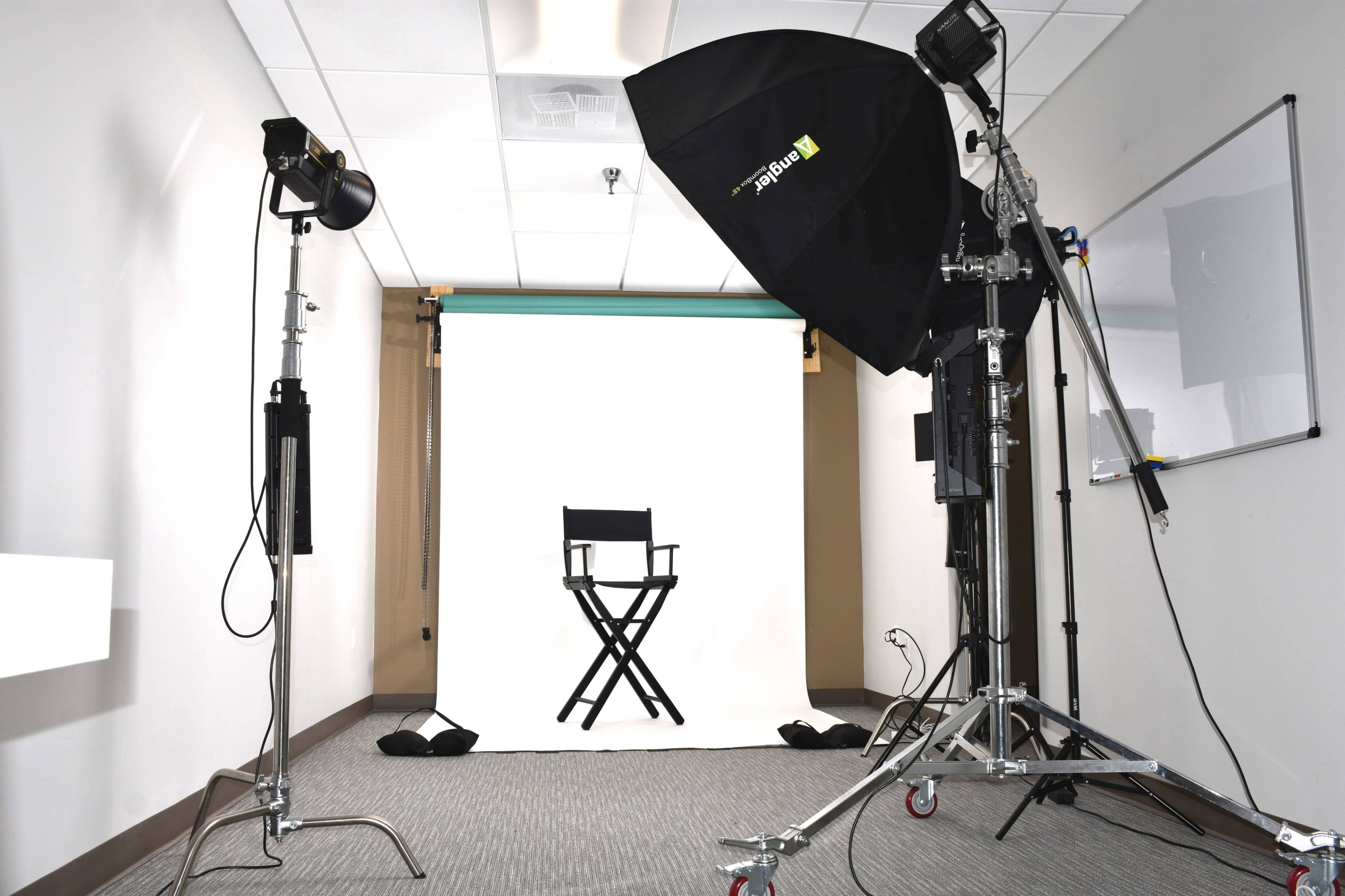 A photography studio setup featuring a blank white backdrop, a director's chair, and professional lighting equipment.