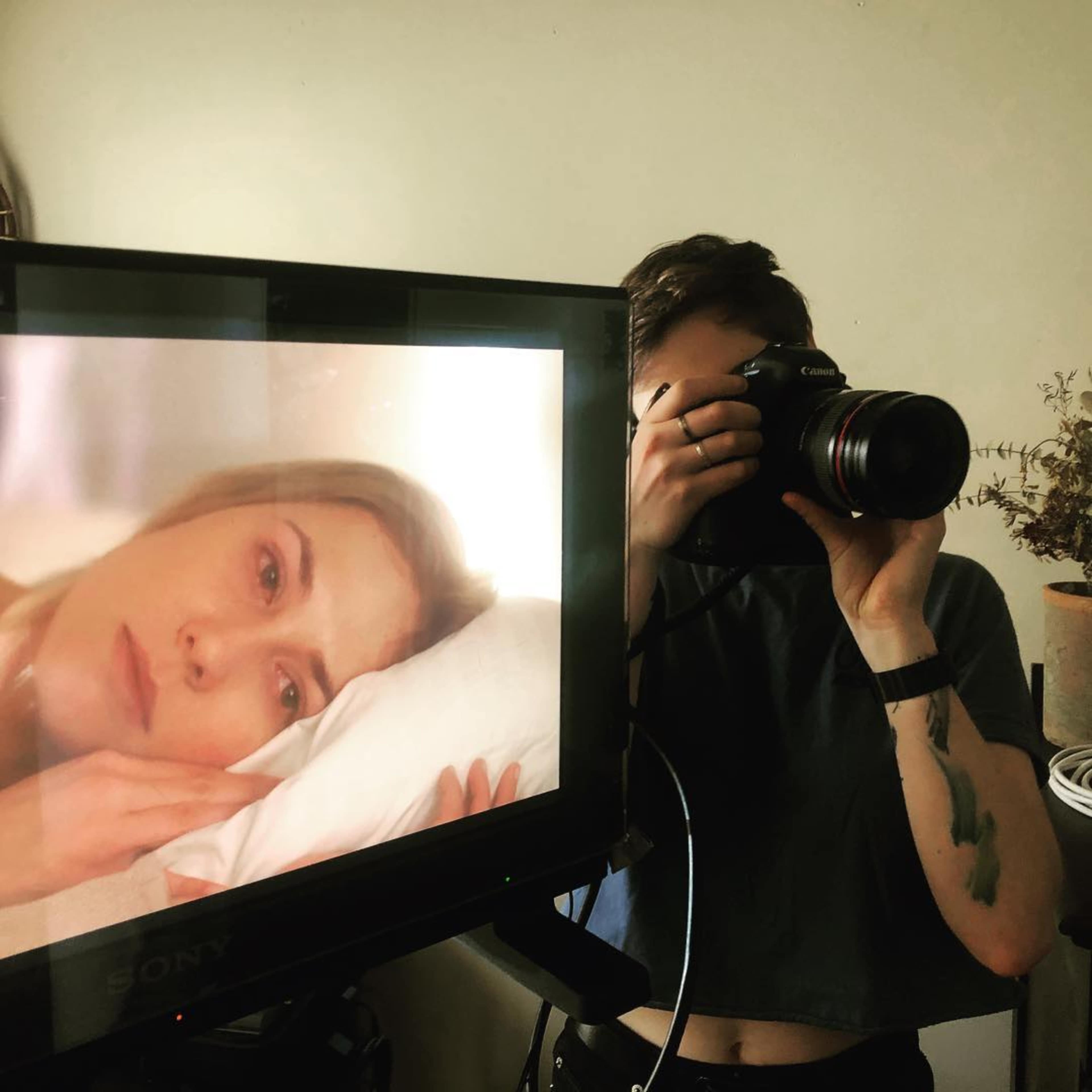 A person holds a camera while photographing a screen displaying a close-up of a woman lying on a pillow.