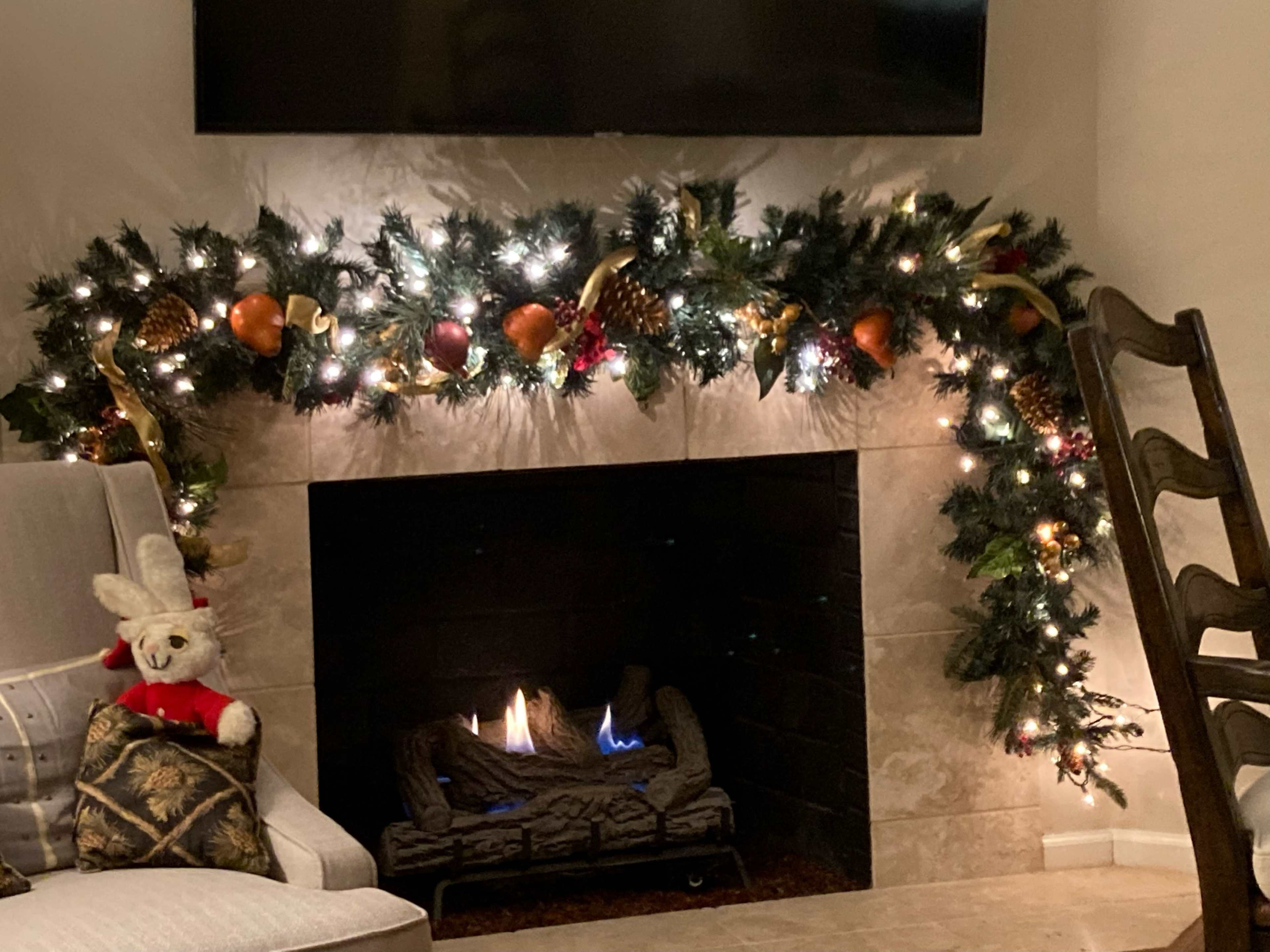A fireplace adorned with a decorative garland featuring lights, pine cones, and ornaments sits within a cozy living room setting.