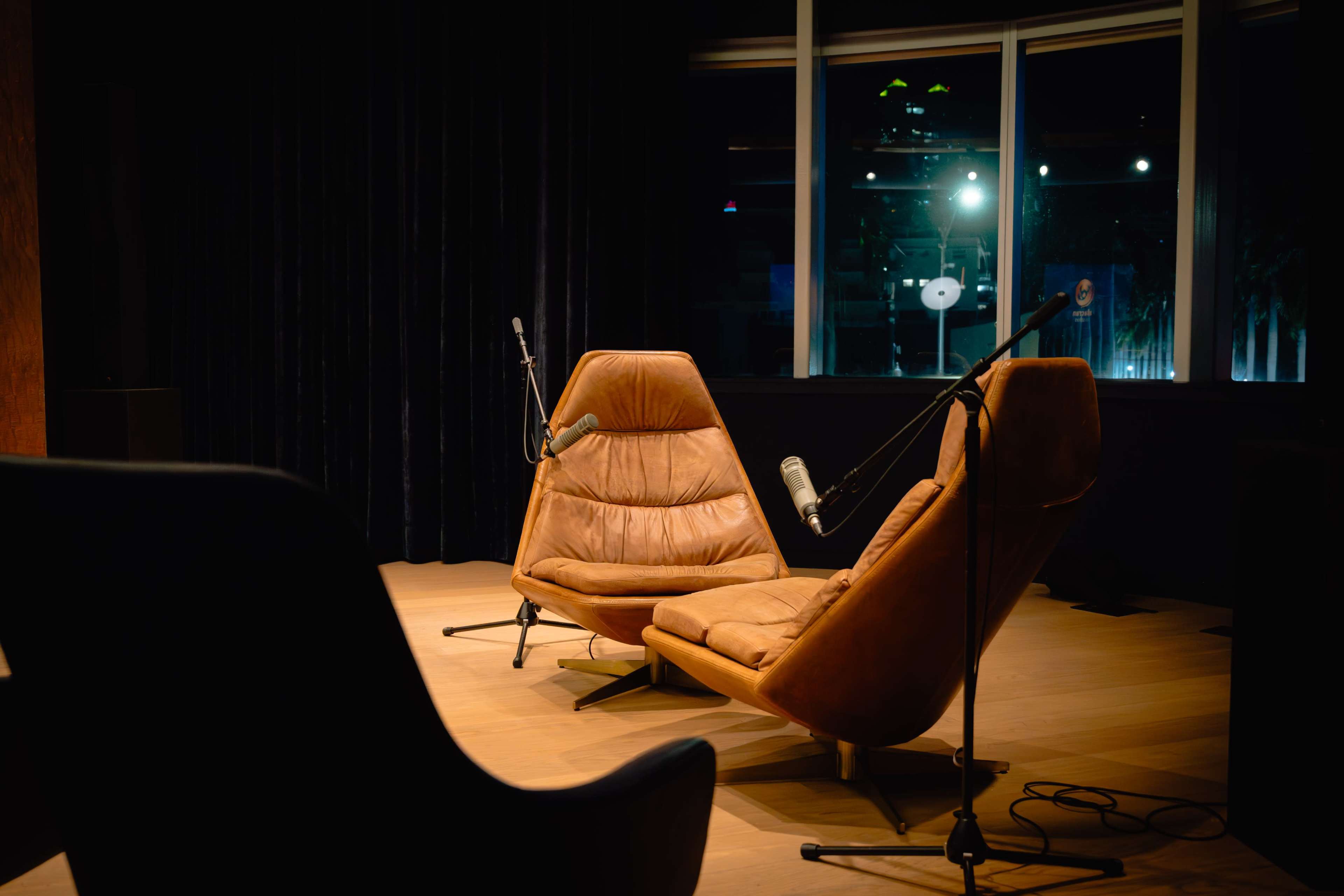 Two modern, brown lounge chairs are positioned facing each other in a dimly lit room, each equipped with a microphone.