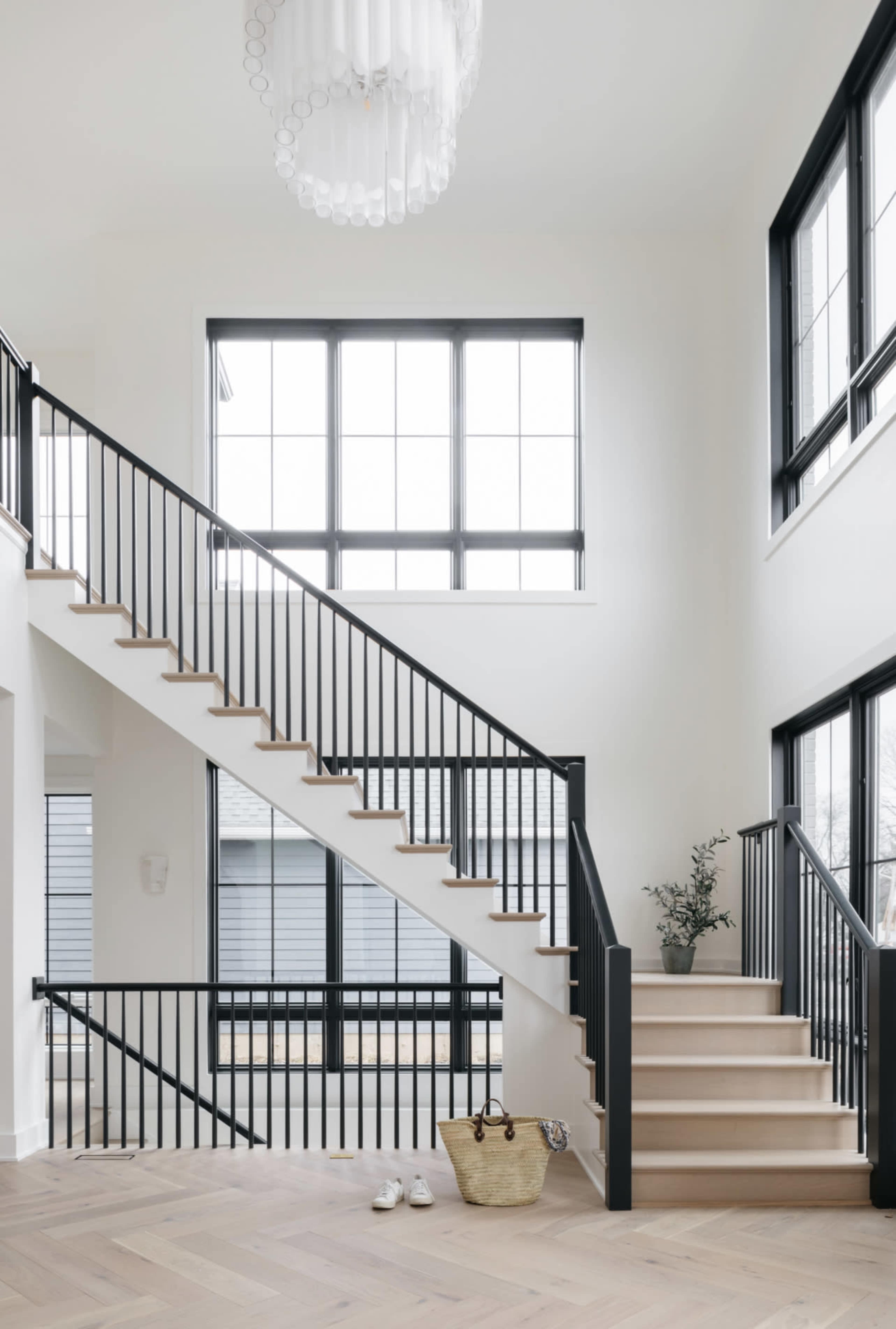 A modern entryway features a staircase with black railings, large windows, and a light fixture hanging from the ceiling.