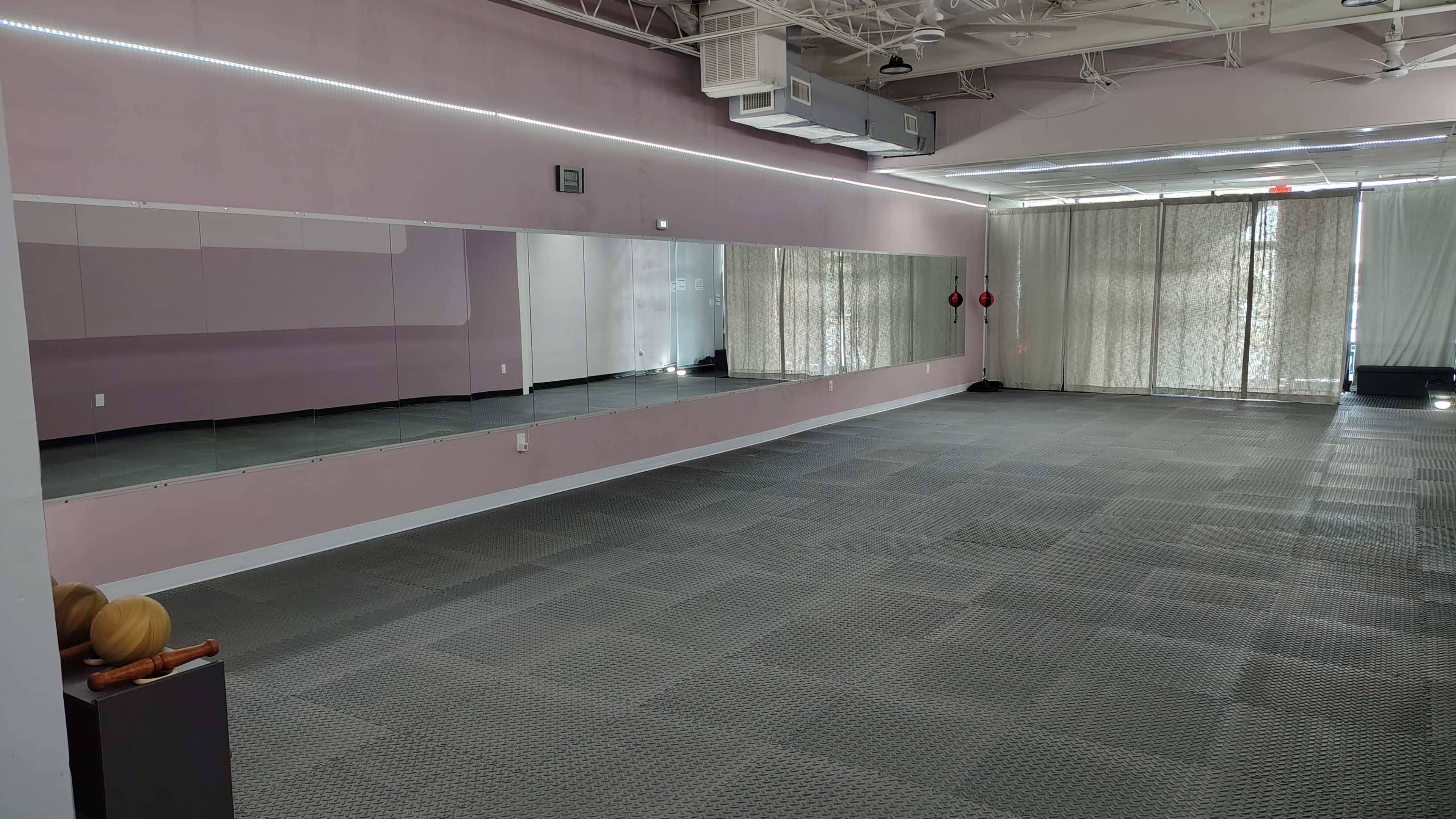 The image shows a spacious, empty room with pink walls, a large mirror on one side, and patterned gray flooring.
