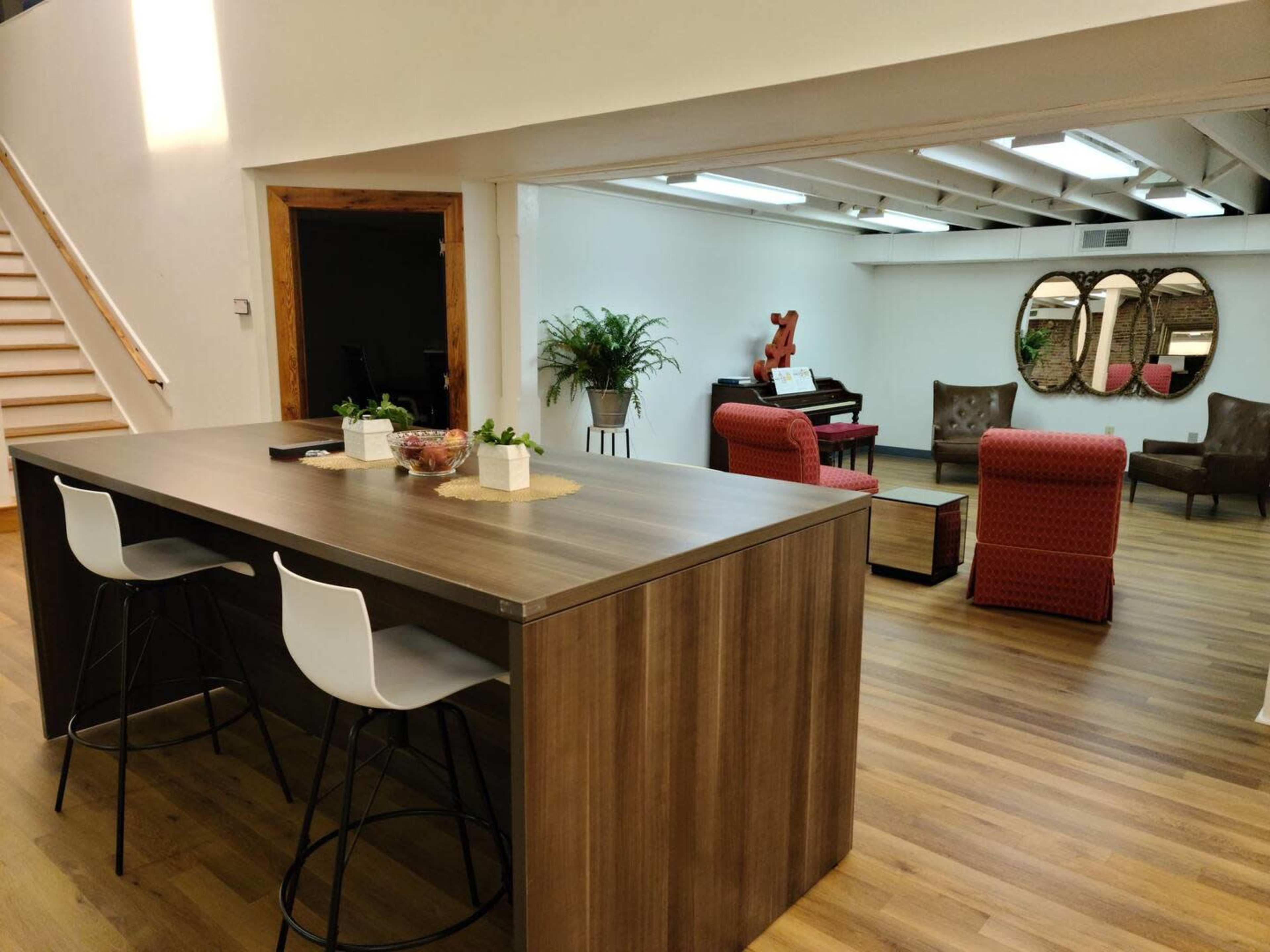 A spacious interior featuring a modern kitchen island with barstools, leading to a cozy seating area furnished with chairs and a piano.