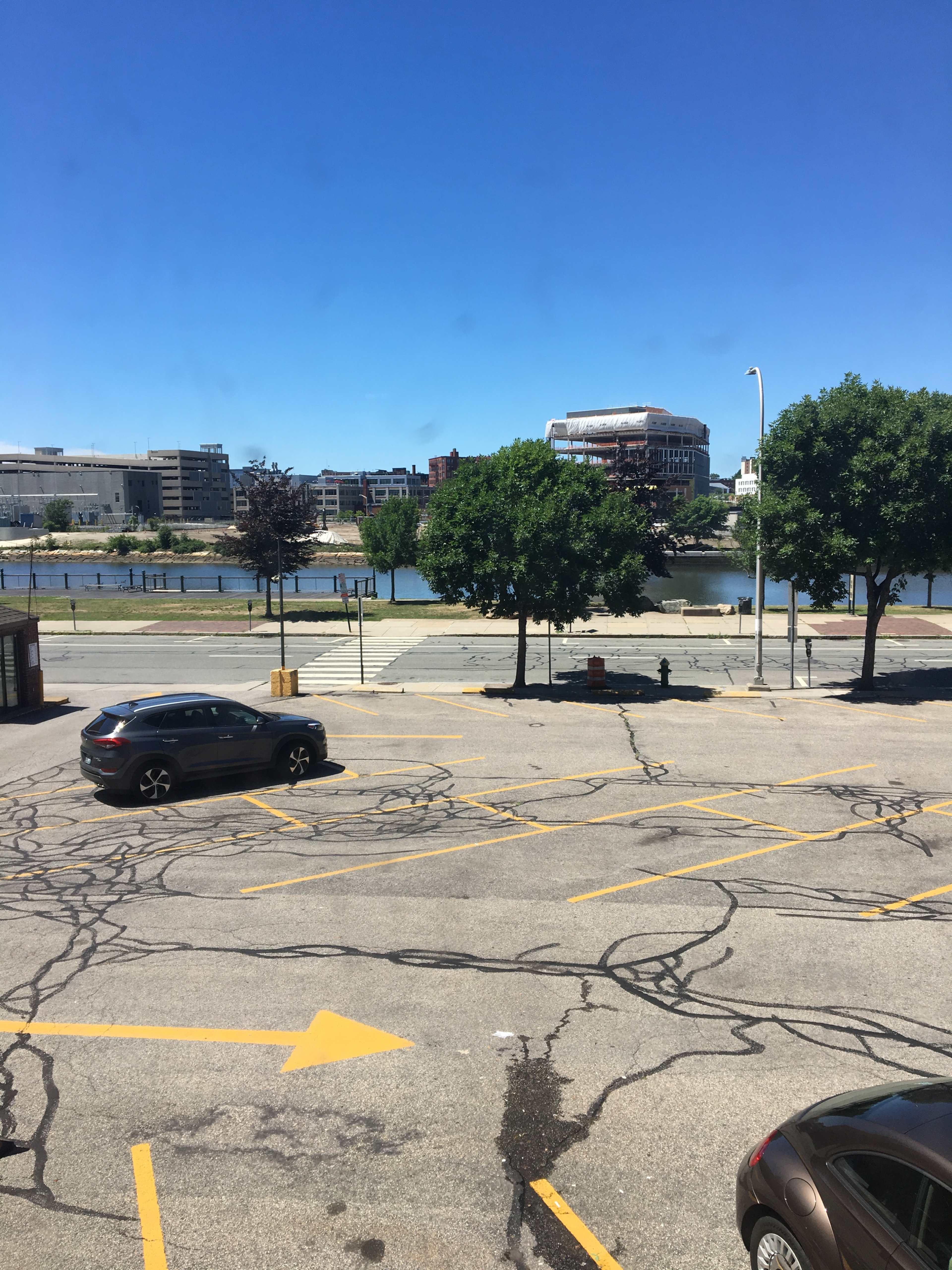 A view of a parking lot with a few cars and a river in the background under clear blue skies.