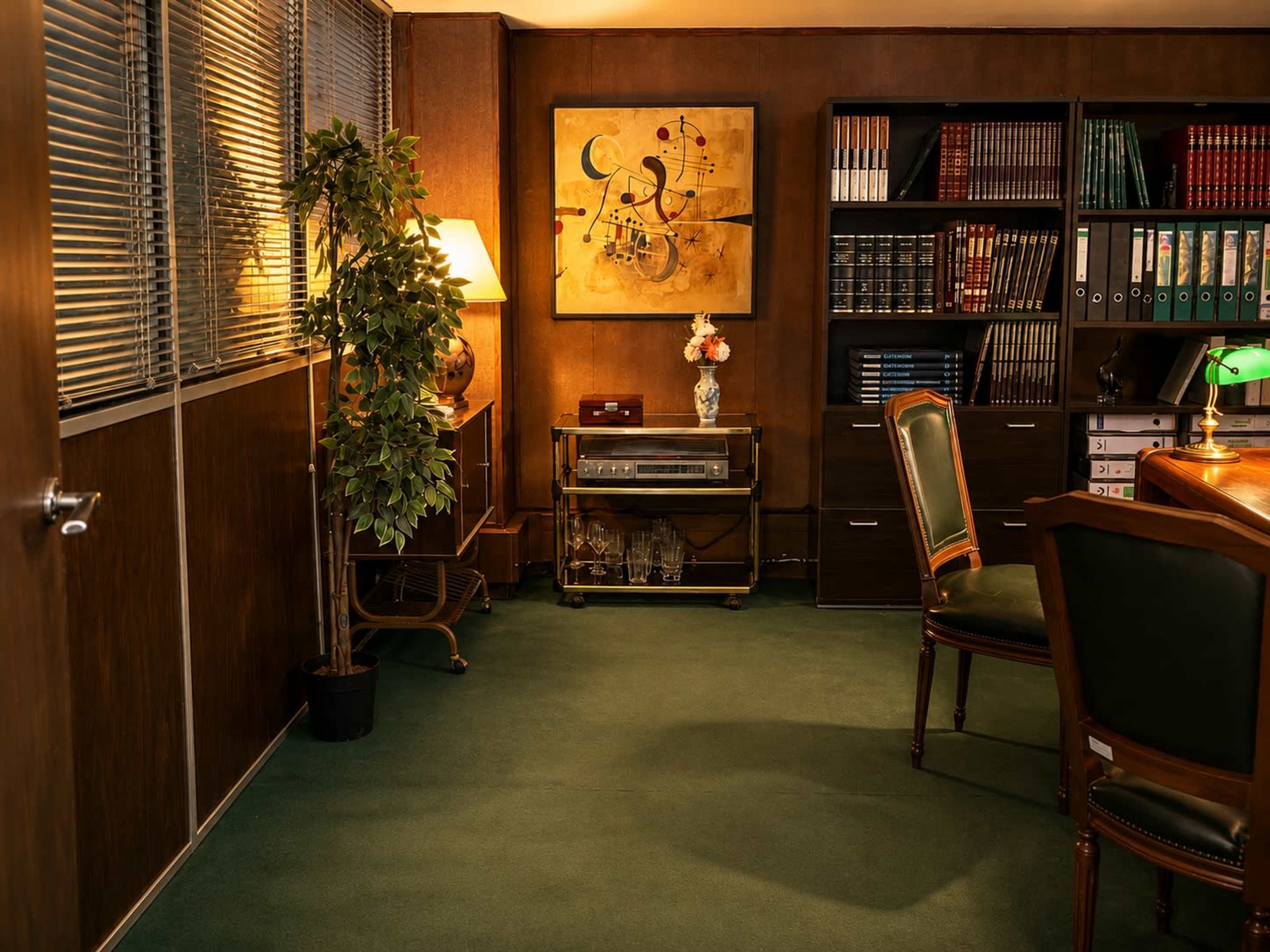 The image shows a well-furnished office with a green carpet, a wooden desk, a decorative plant, bookshelves, and a piece of abstract art on the wall.
