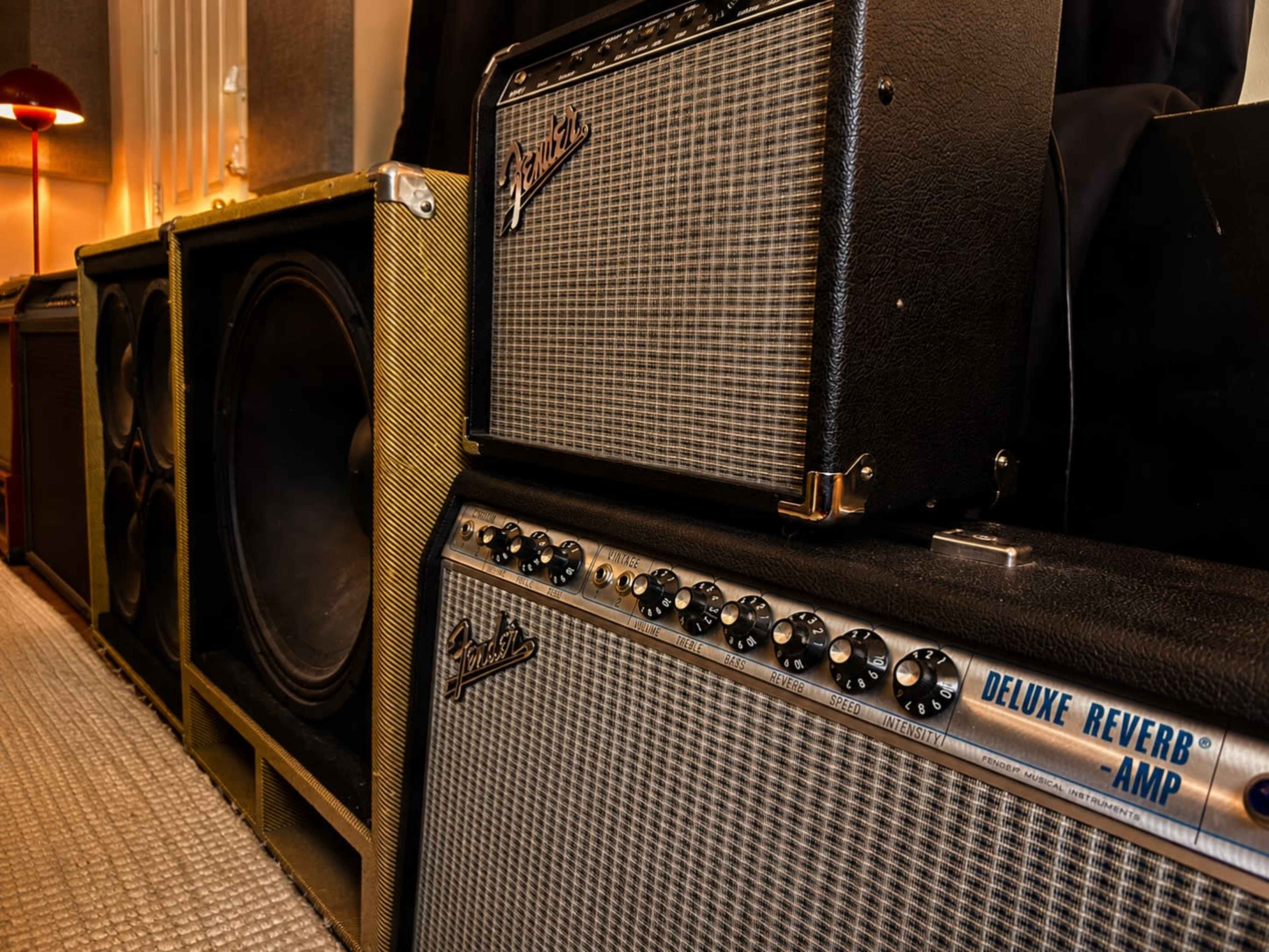 The image features a row of vintage guitar amplifiers and speakers lined up against a wall.