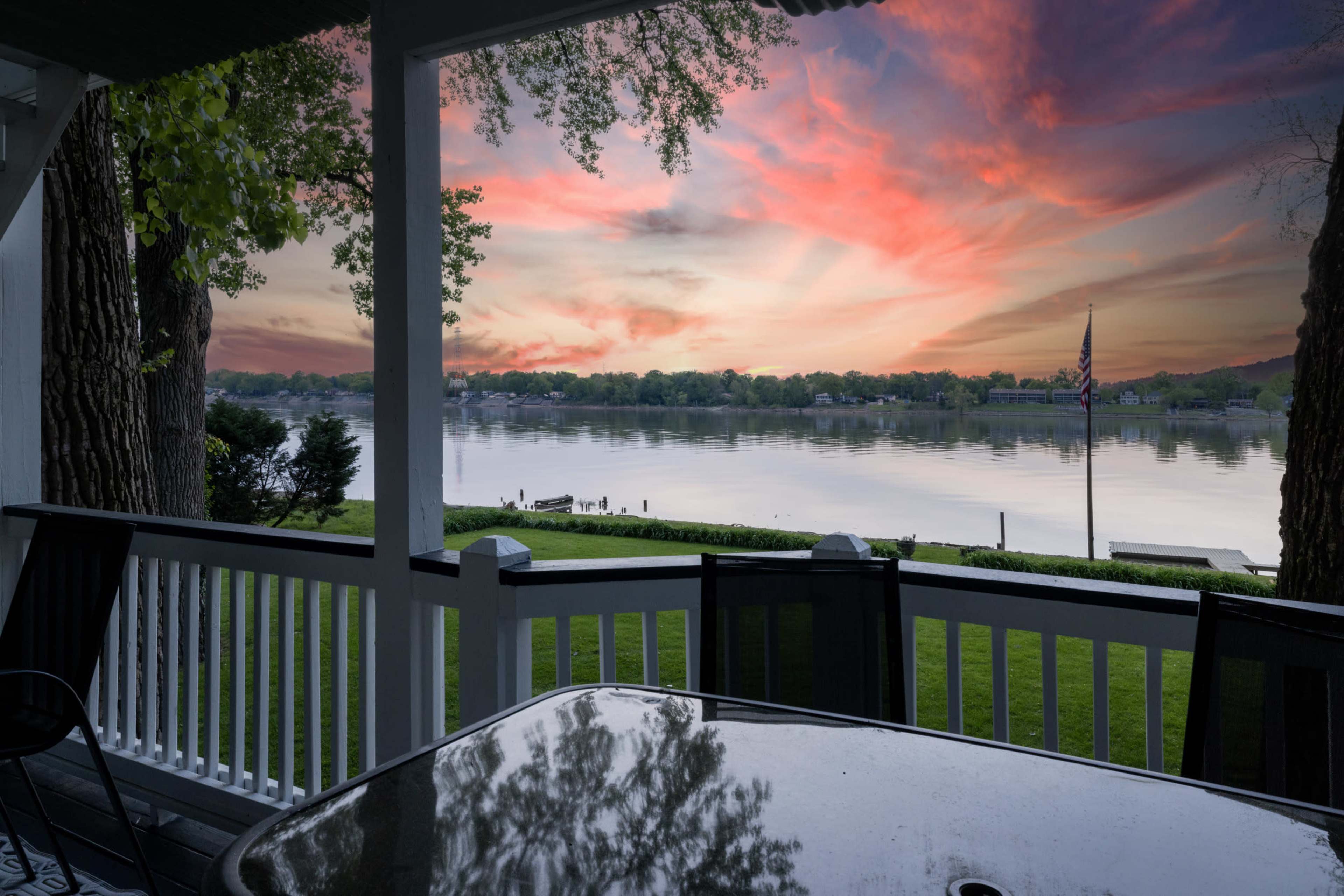 The image shows a scenic view of a lake at sunset, framed by a porch railing and a table in the foreground.
