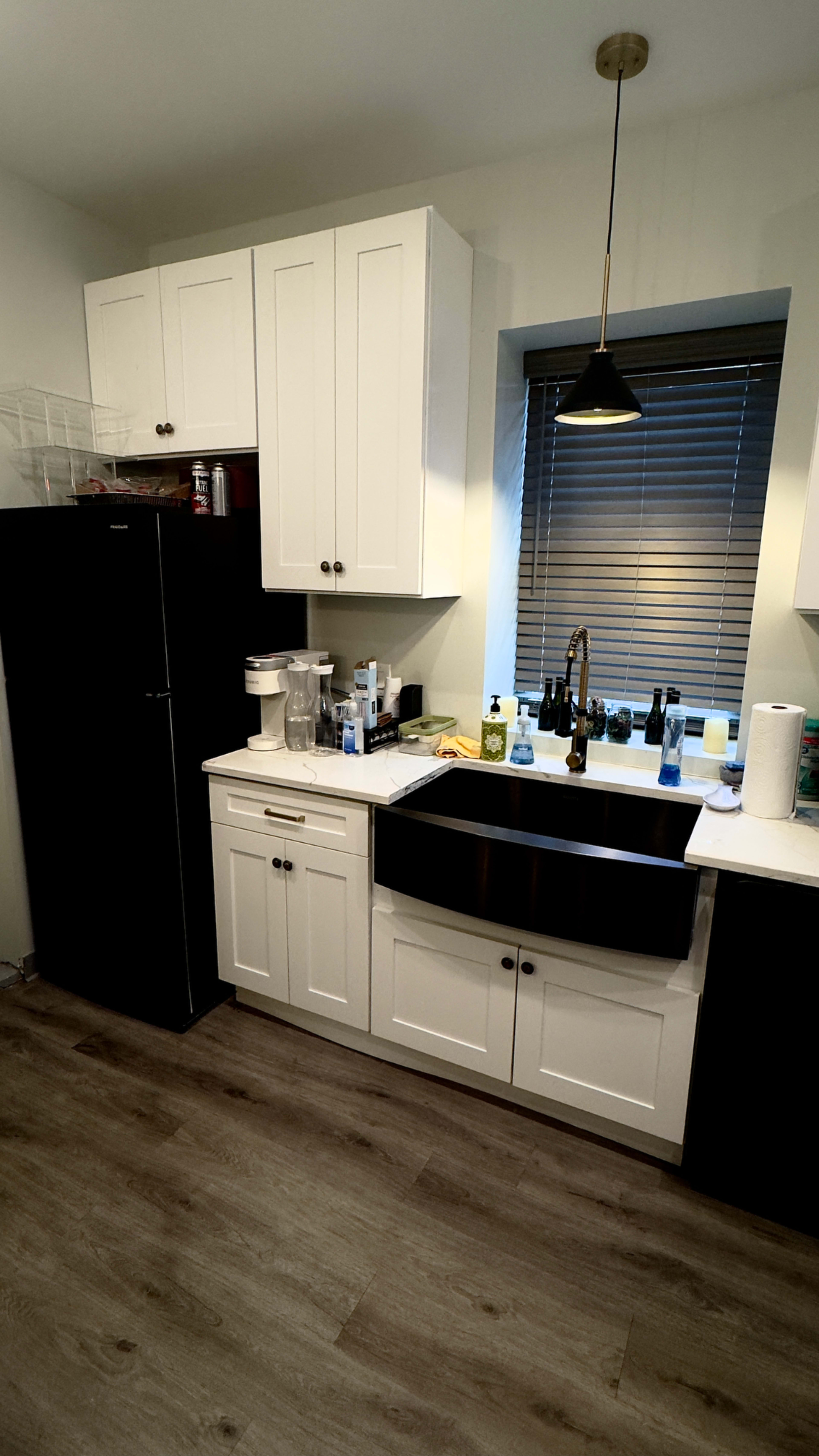 The image shows a kitchen featuring black cabinets, a stainless steel sink, and a window with white blinds.