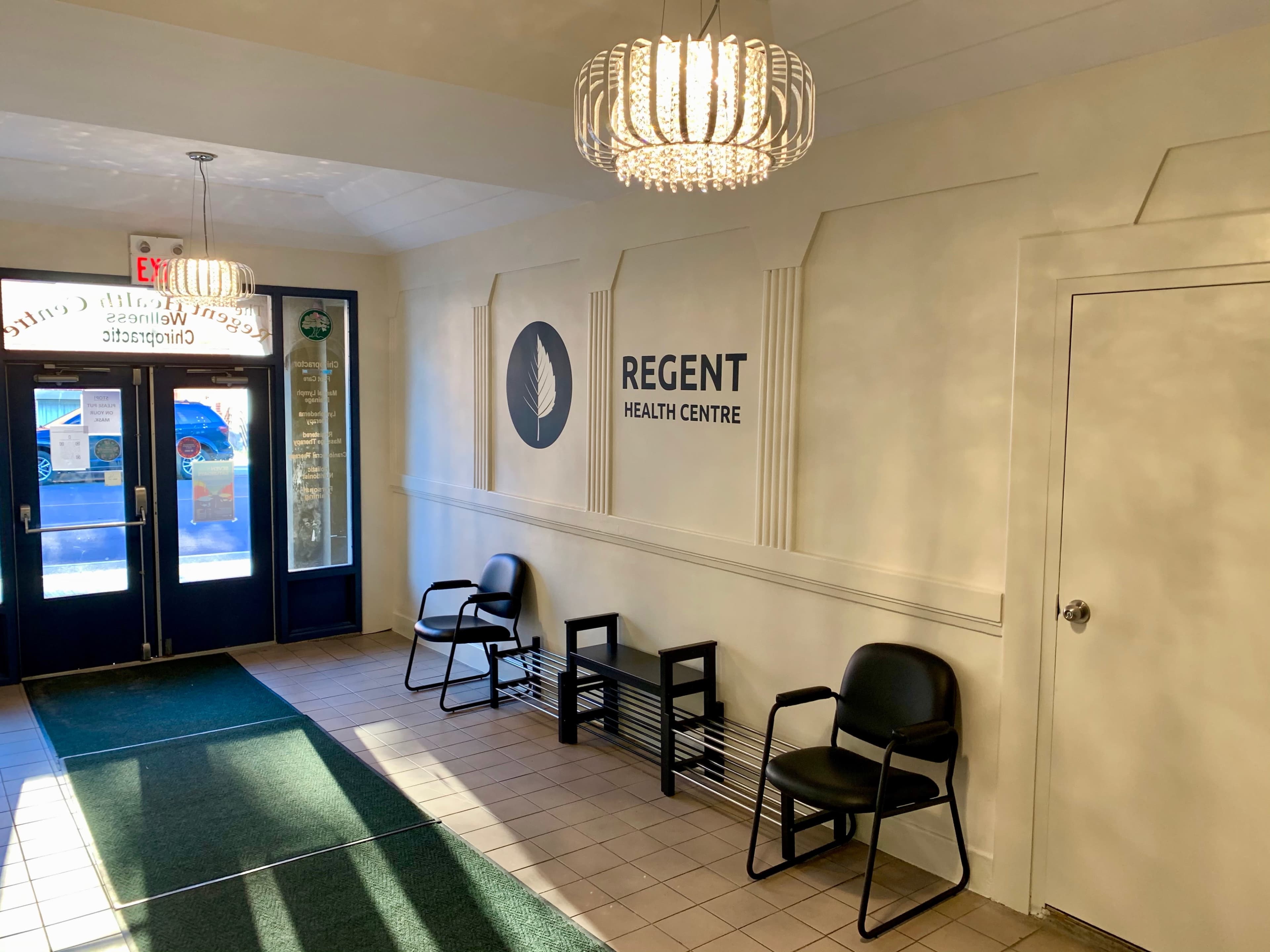 The entrance of Regent Health Centre features chairs against a wall with the center's logo and two modern light fixtures above.