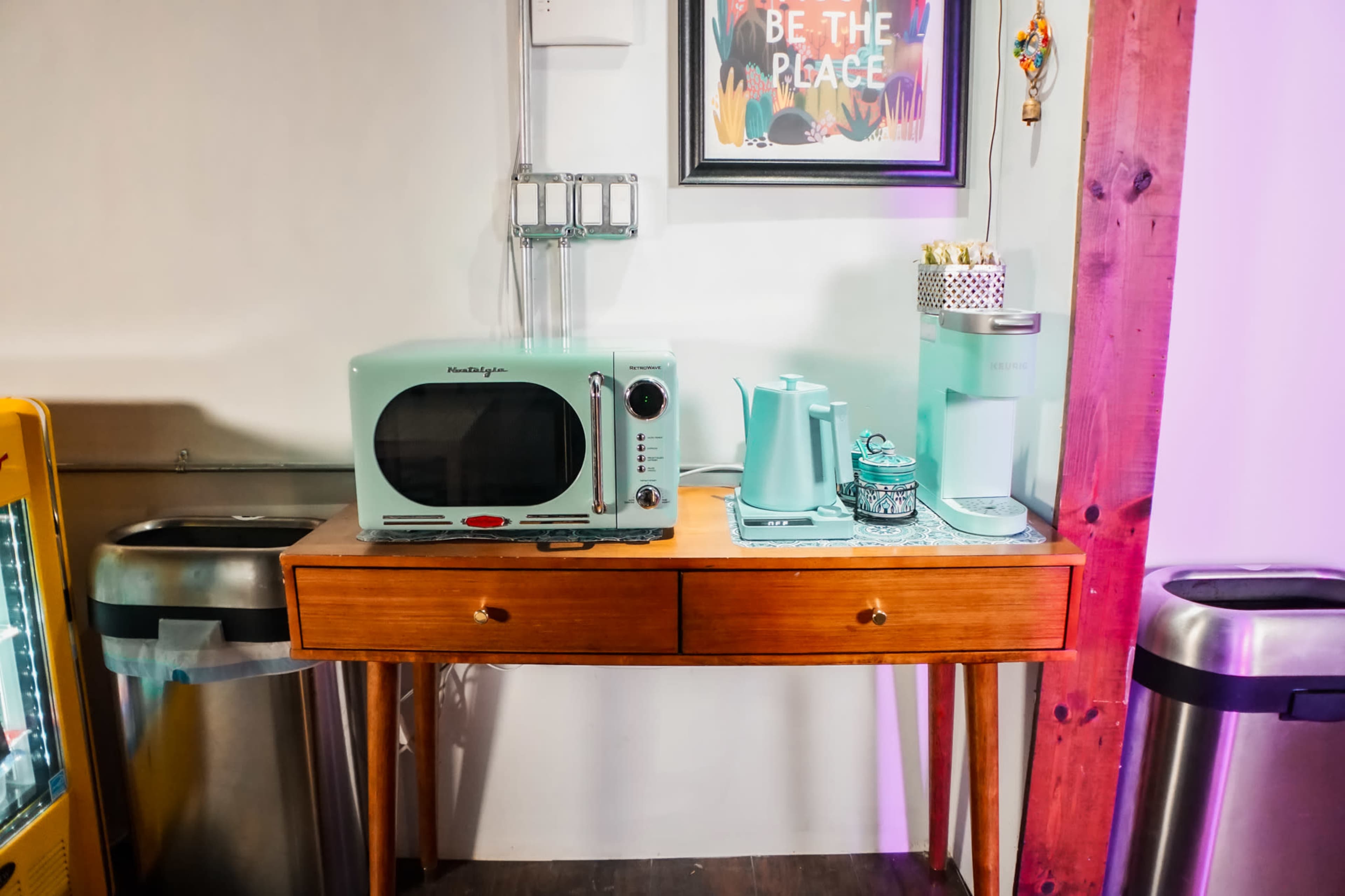 A retro-style microwave and kettle, along with a metal container, are displayed on a wooden table against a wall.