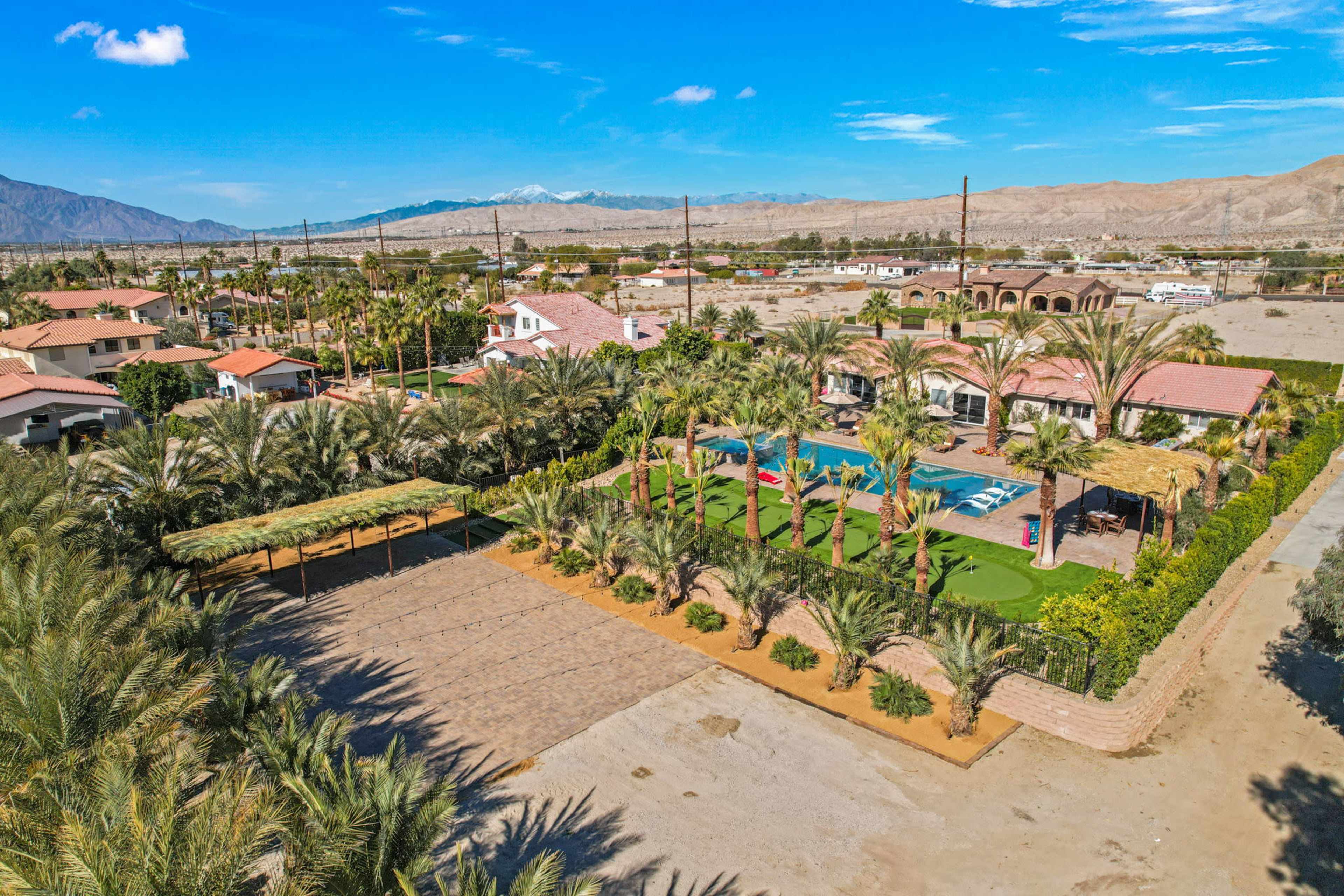 A resort-like setting featuring a swimming pool, palm trees, and landscaped areas surrounded by residential buildings and mountains in the background.