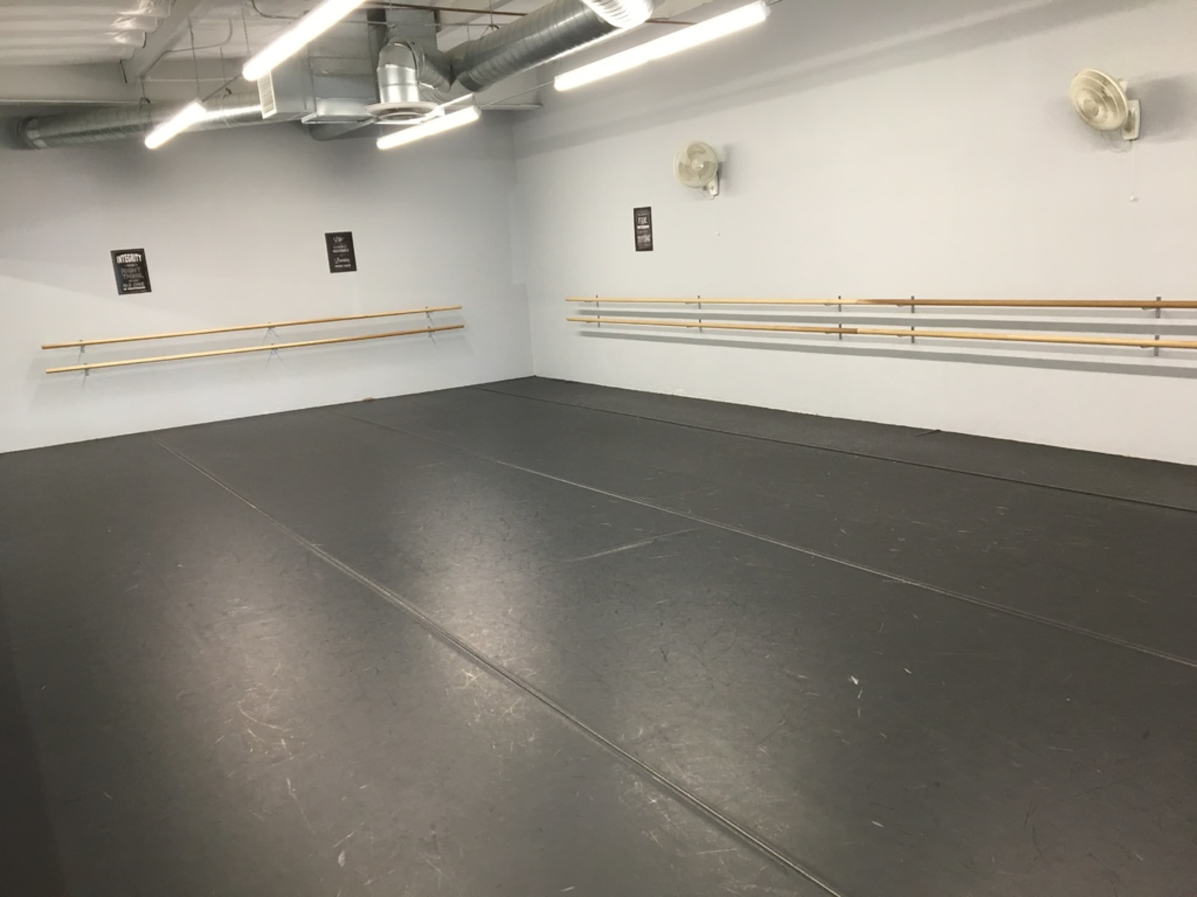 The image shows an empty dance studio with wooden ballet barres attached to the walls and a smooth, dark flooring surface.
