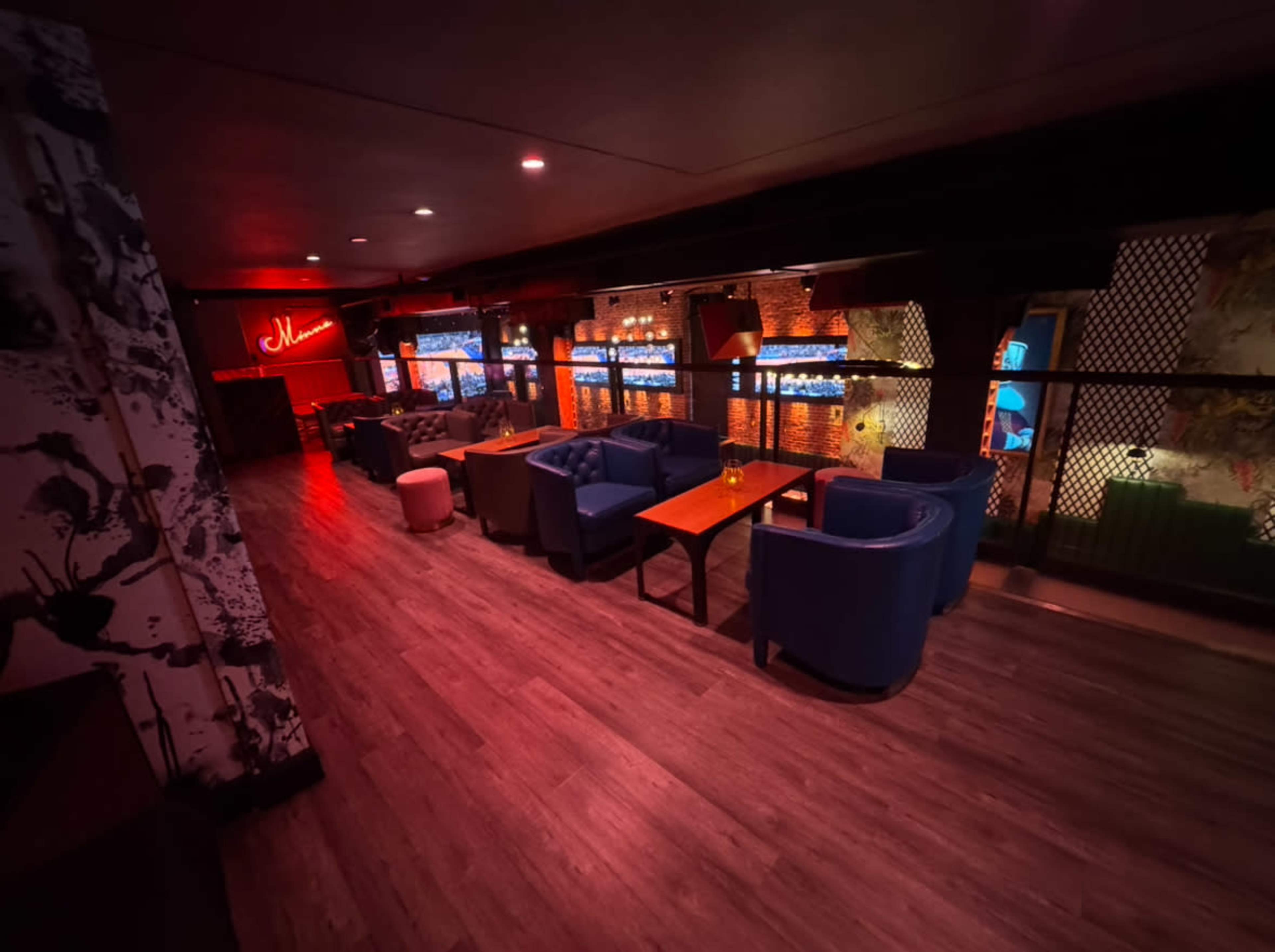 The image shows a dimly lit lounge area with blue seating, wooden tables, and illuminated decor.