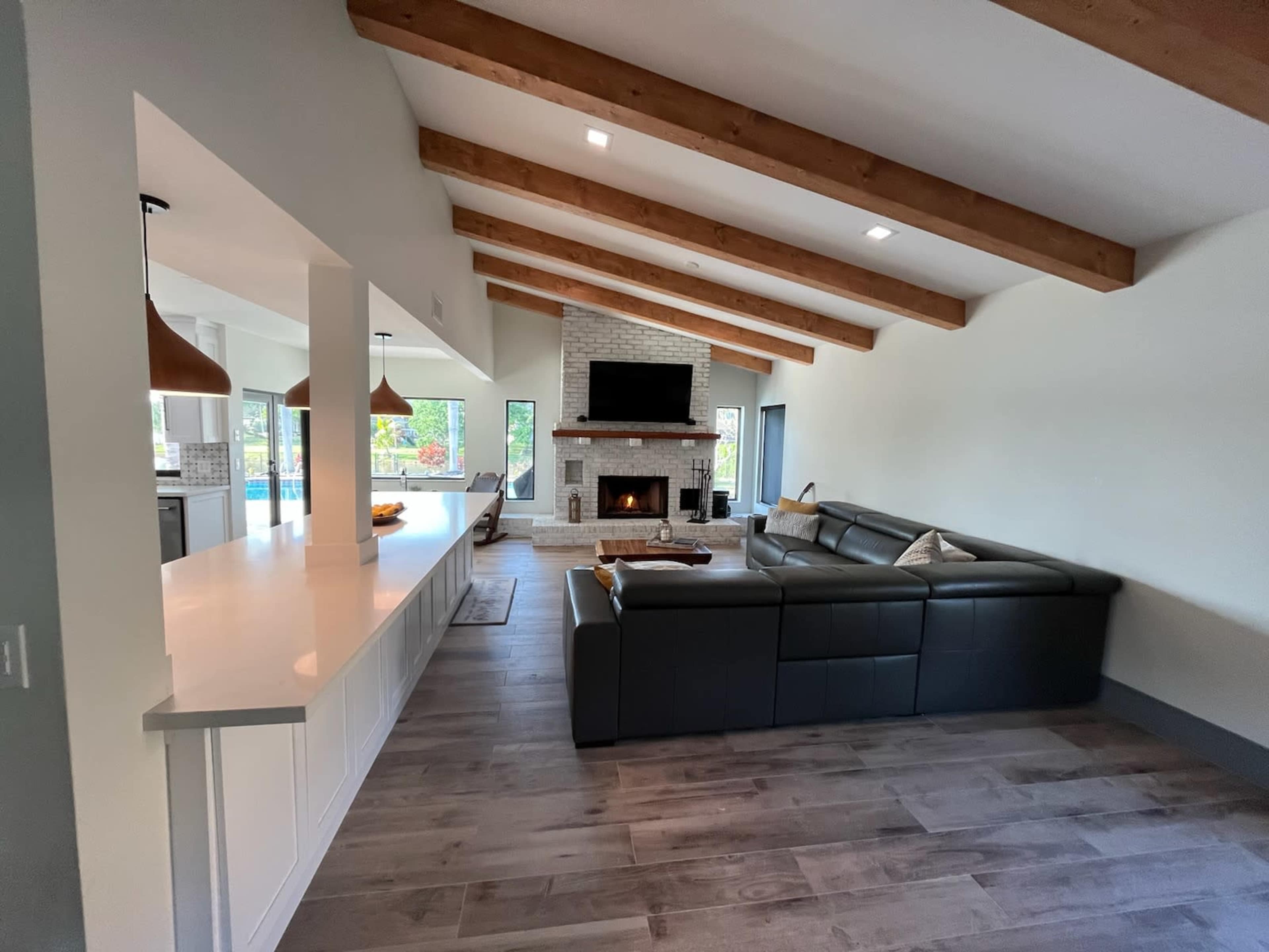 A spacious living room features a dark sectional sofa, a stone fireplace with a mounted television above, and large windows that provide natural light.