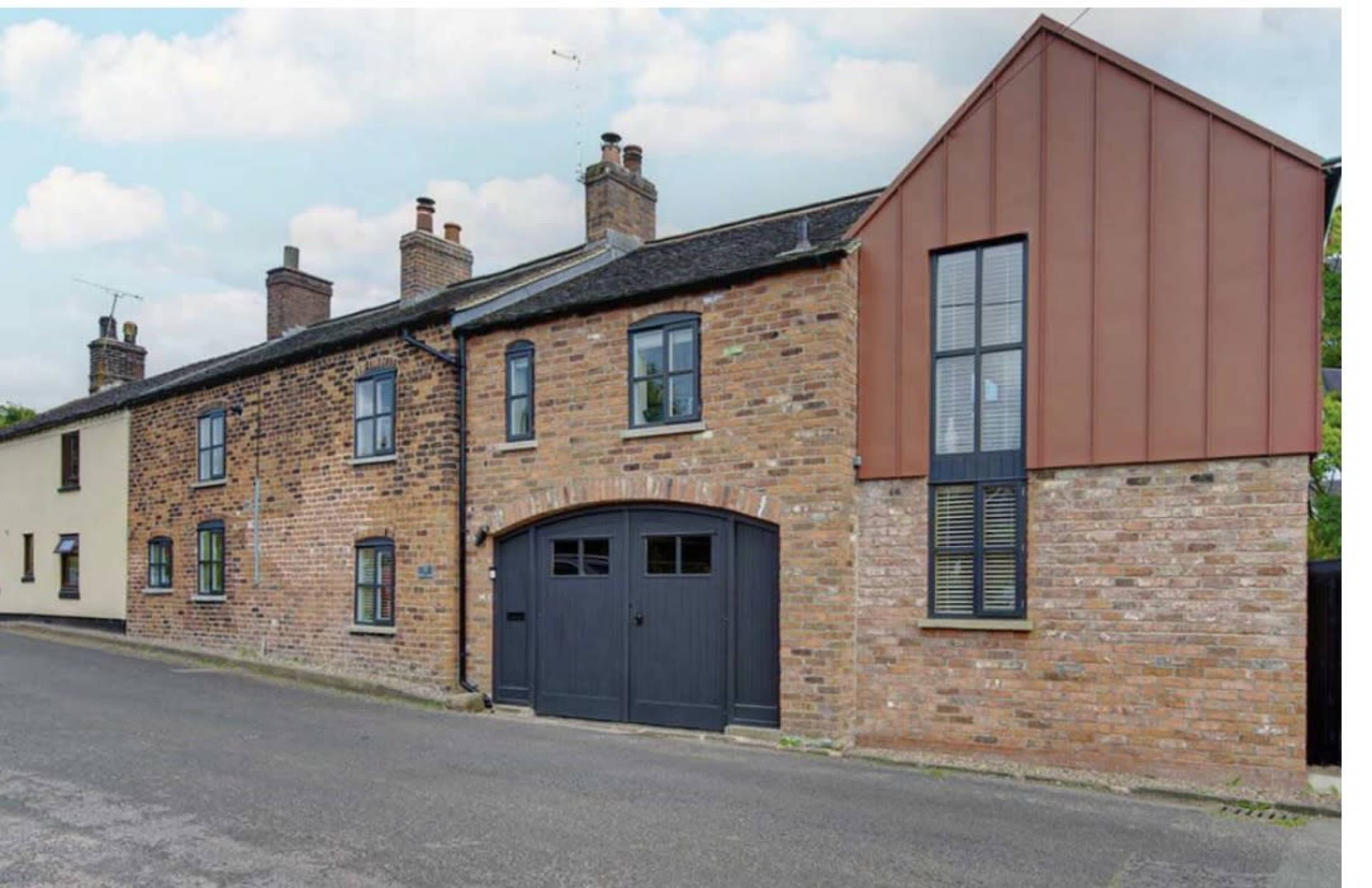 The image shows a brick building featuring a mix of traditional and modern architectural elements, including a dark garage door and large windows.