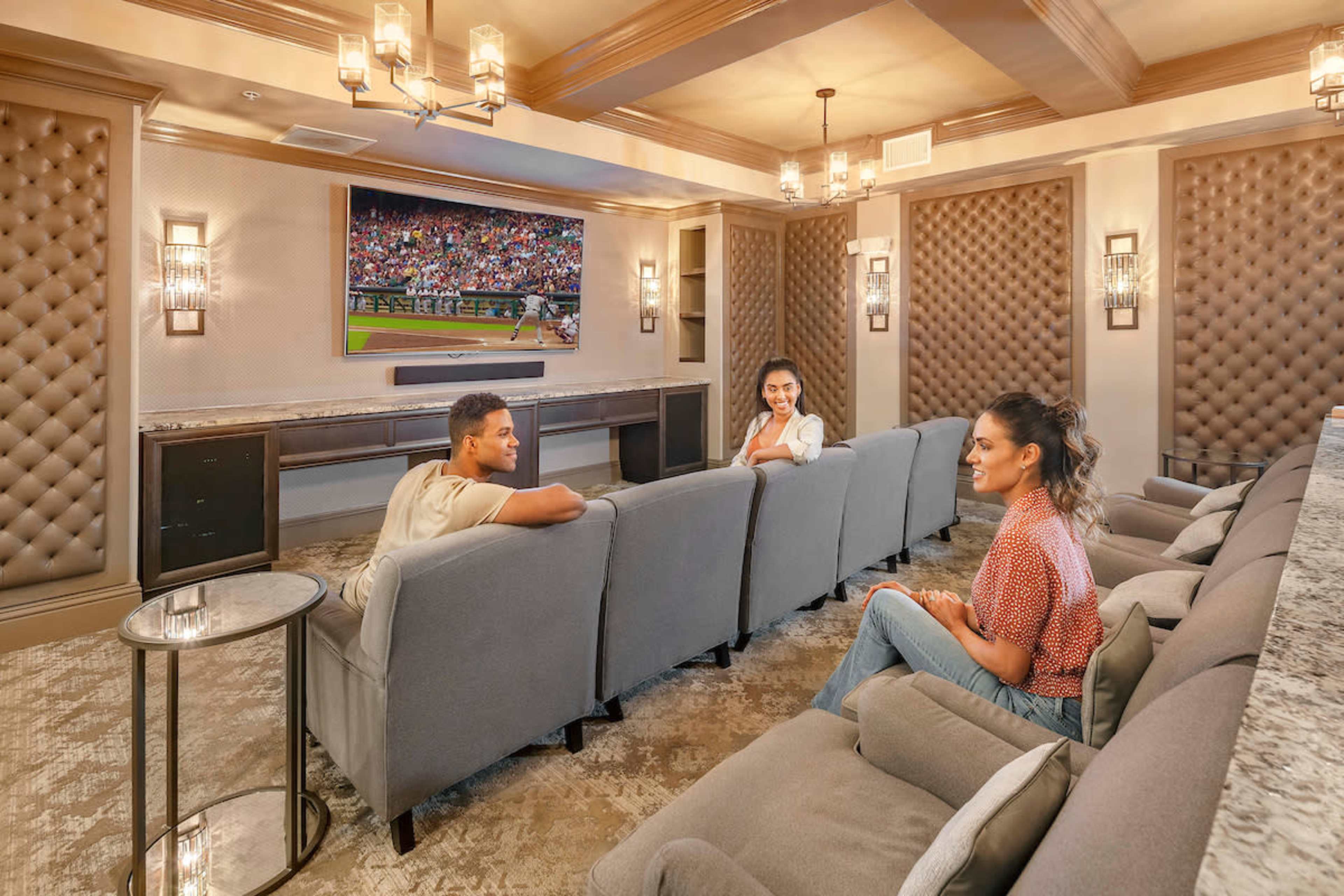 Three people are seated in a well-decorated media room watching a baseball game on a large screen.