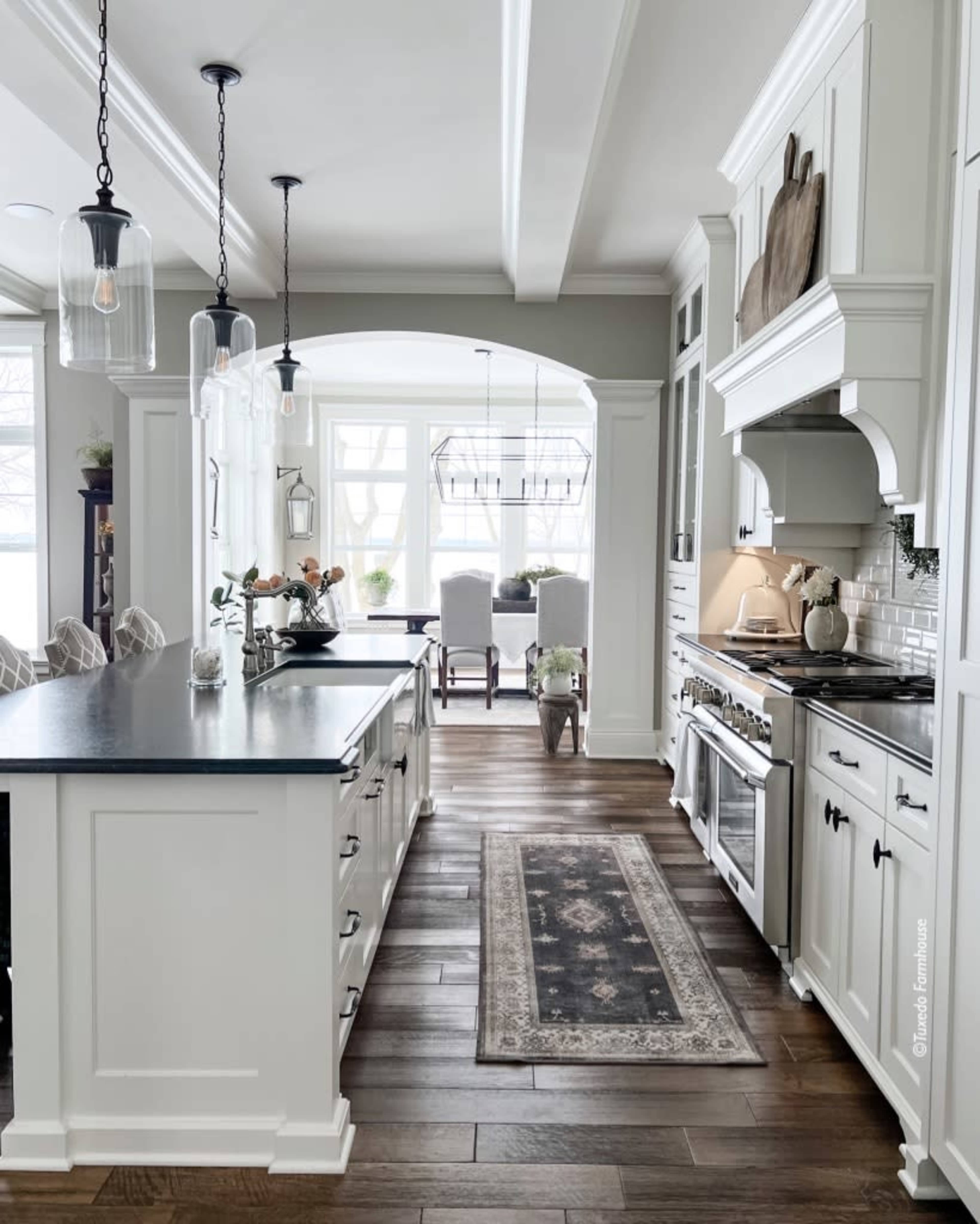 A modern kitchen with a central island, pendant lighting, and a dining area visible through an archway.