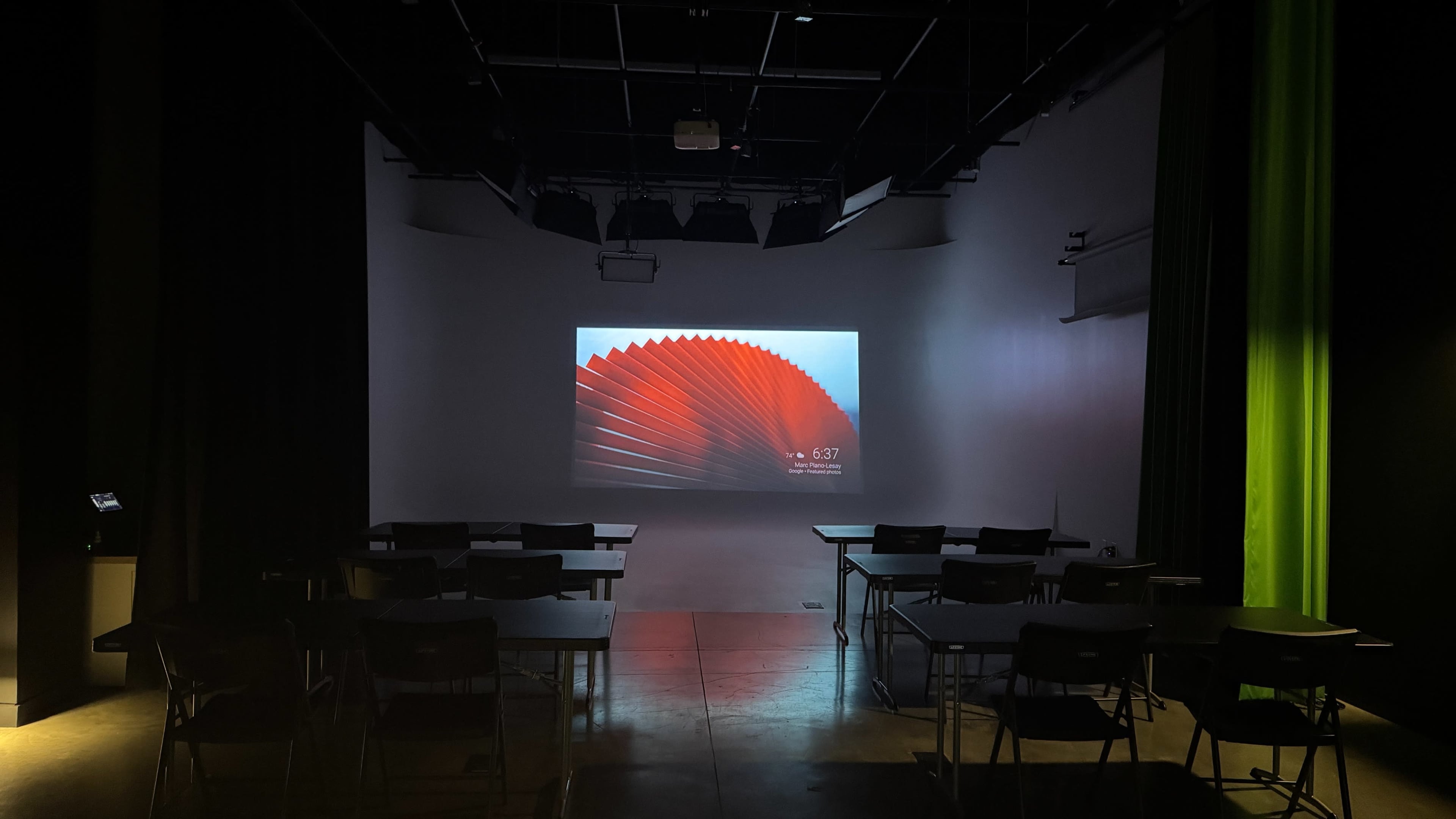 The image shows an empty classroom setting with rows of desks facing a large screen displaying a red abstract design.