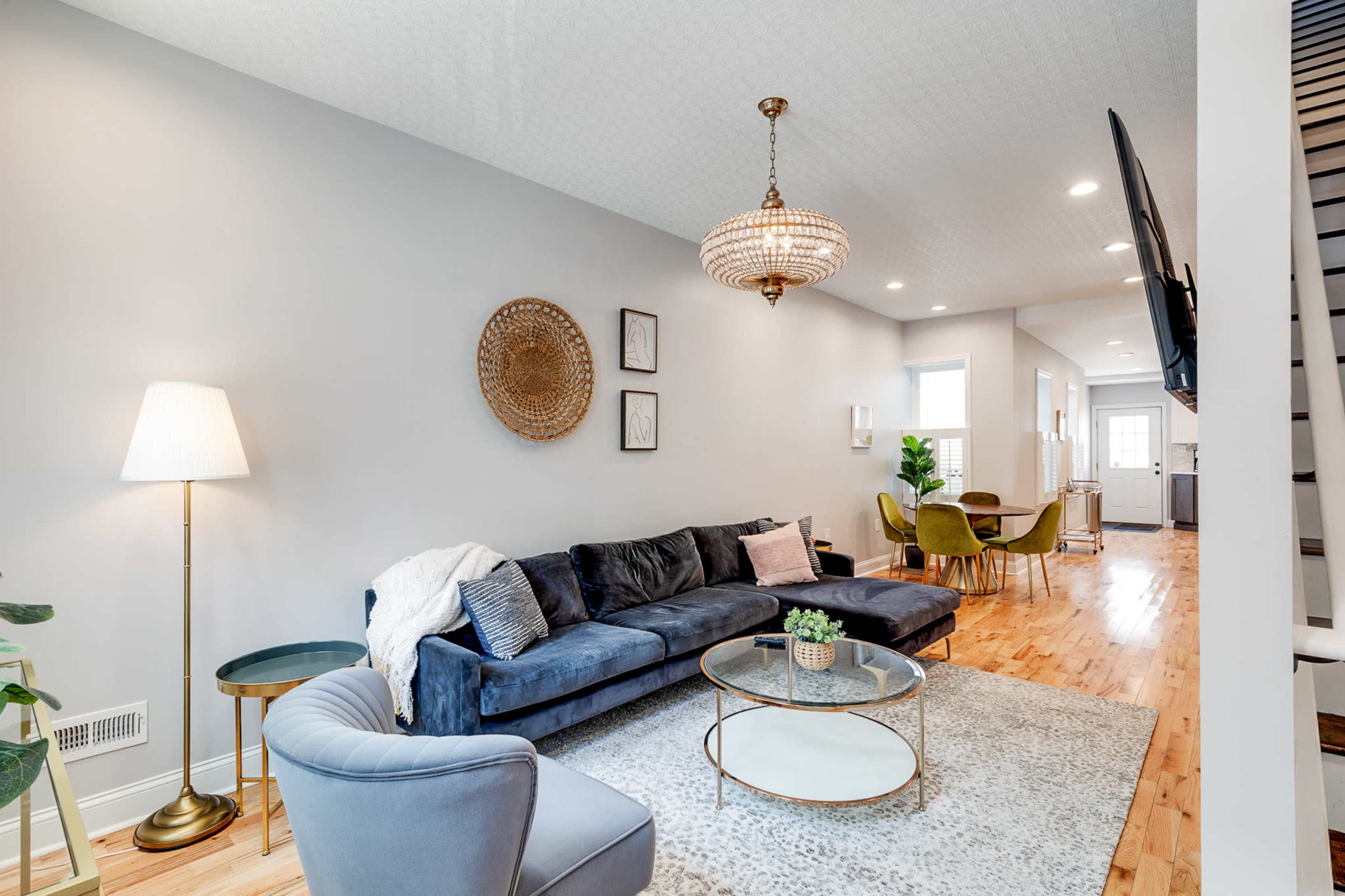 The living room features a blue sectional sofa, a round coffee table, and various decorative elements, including a chandelier and a wall-mounted television.