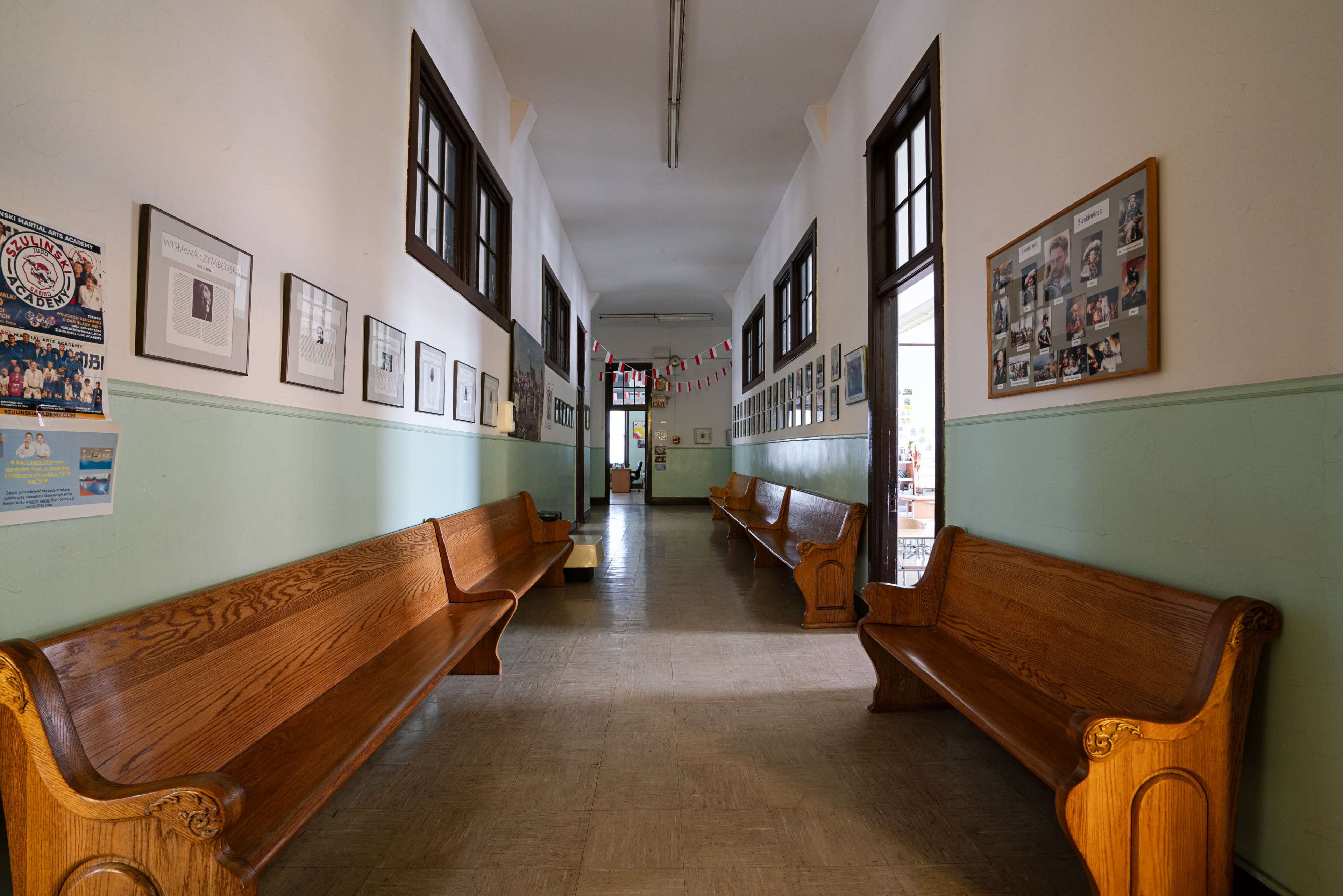 A long hallway with wooden benches on either side, lined with framed photographs on the walls.