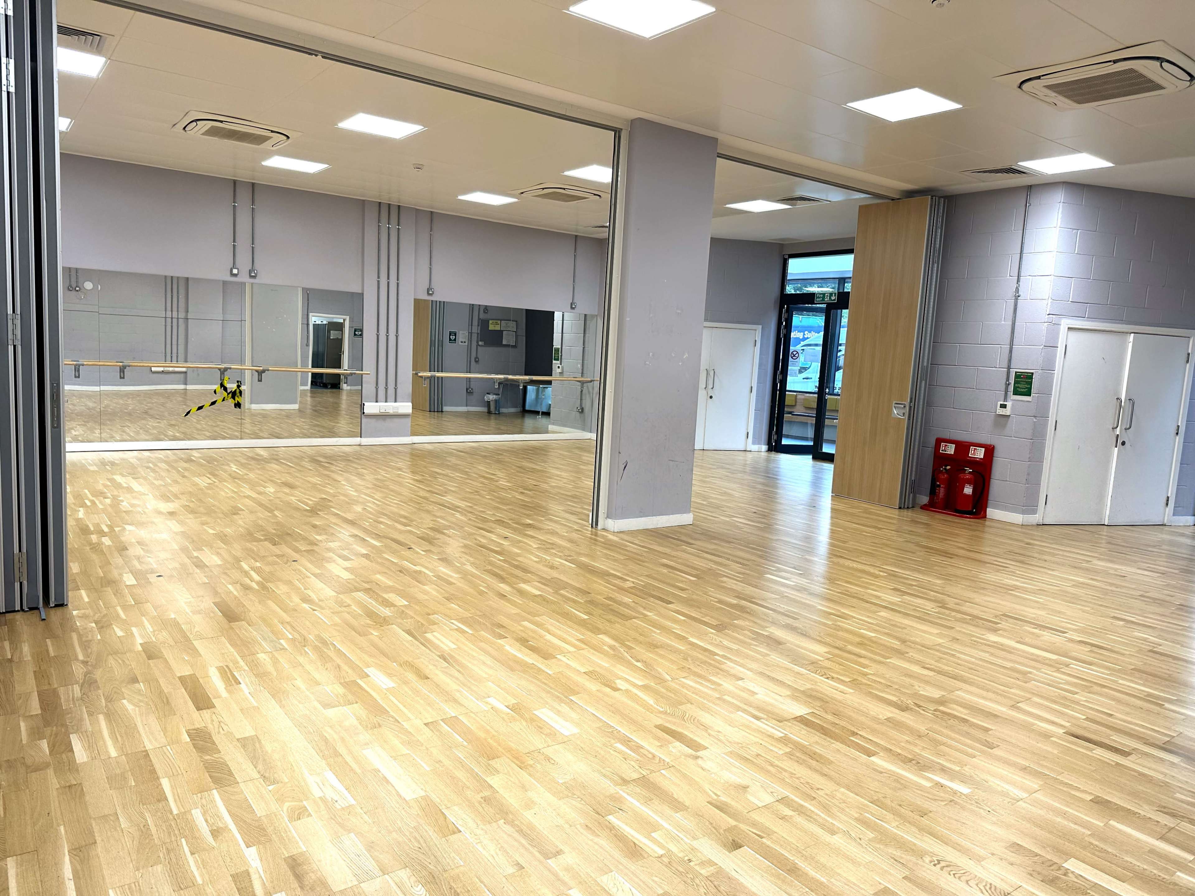 An empty dance studio with wooden flooring and mirrors along one wall.