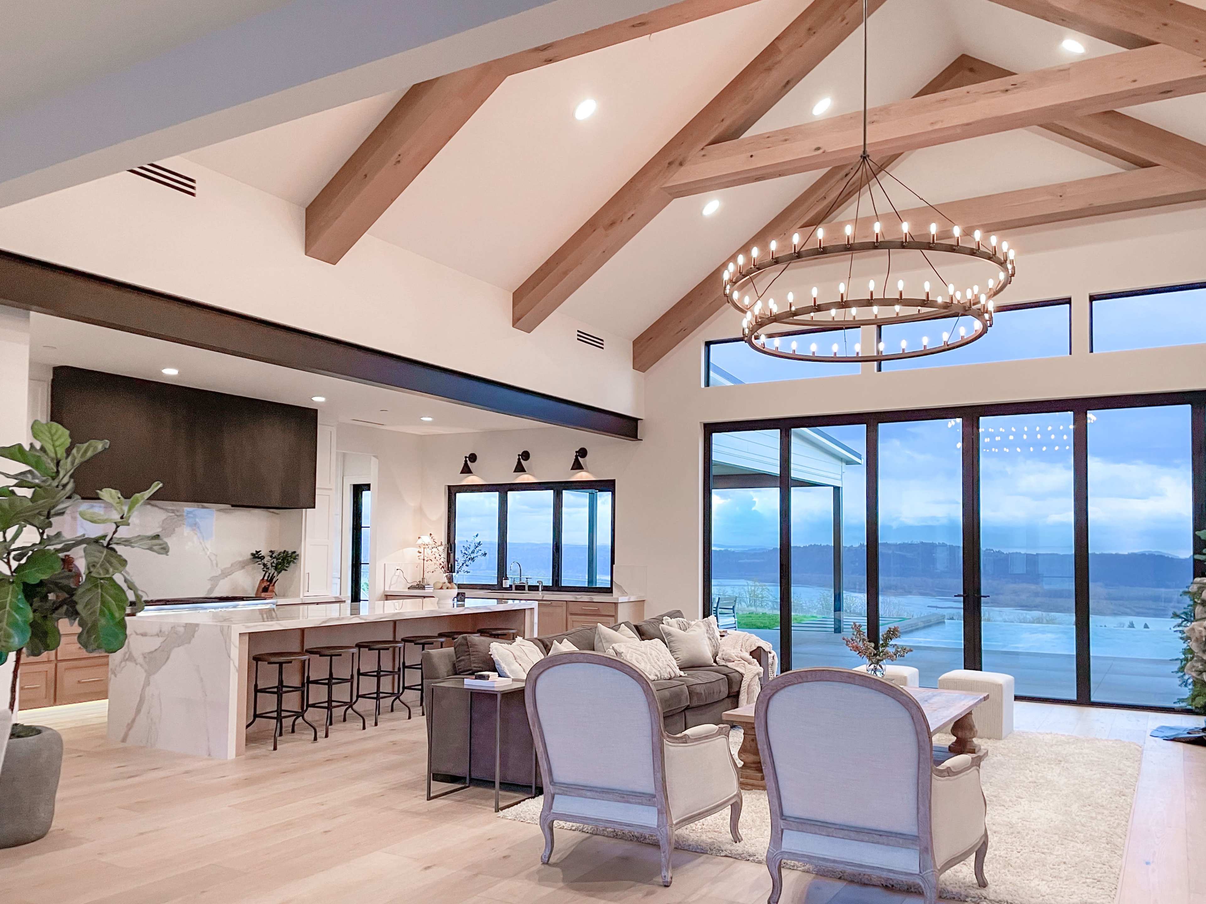 A spacious living area with large windows, wooden beams, and a modern kitchen featuring a marble island.