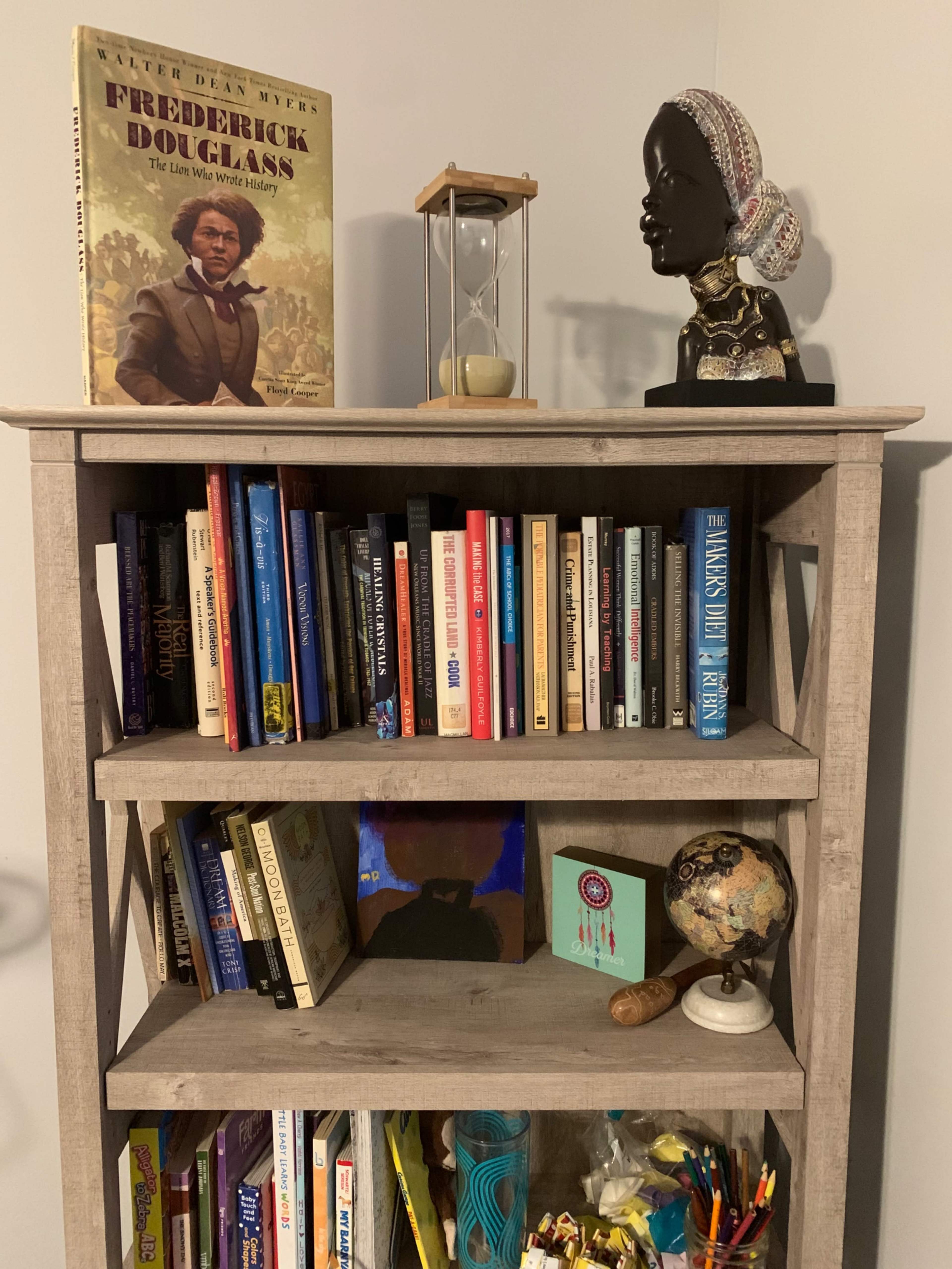 A wooden bookshelf displays a collection of books, a globe, an hourglass, and decorative items, including a bust and a portrait.