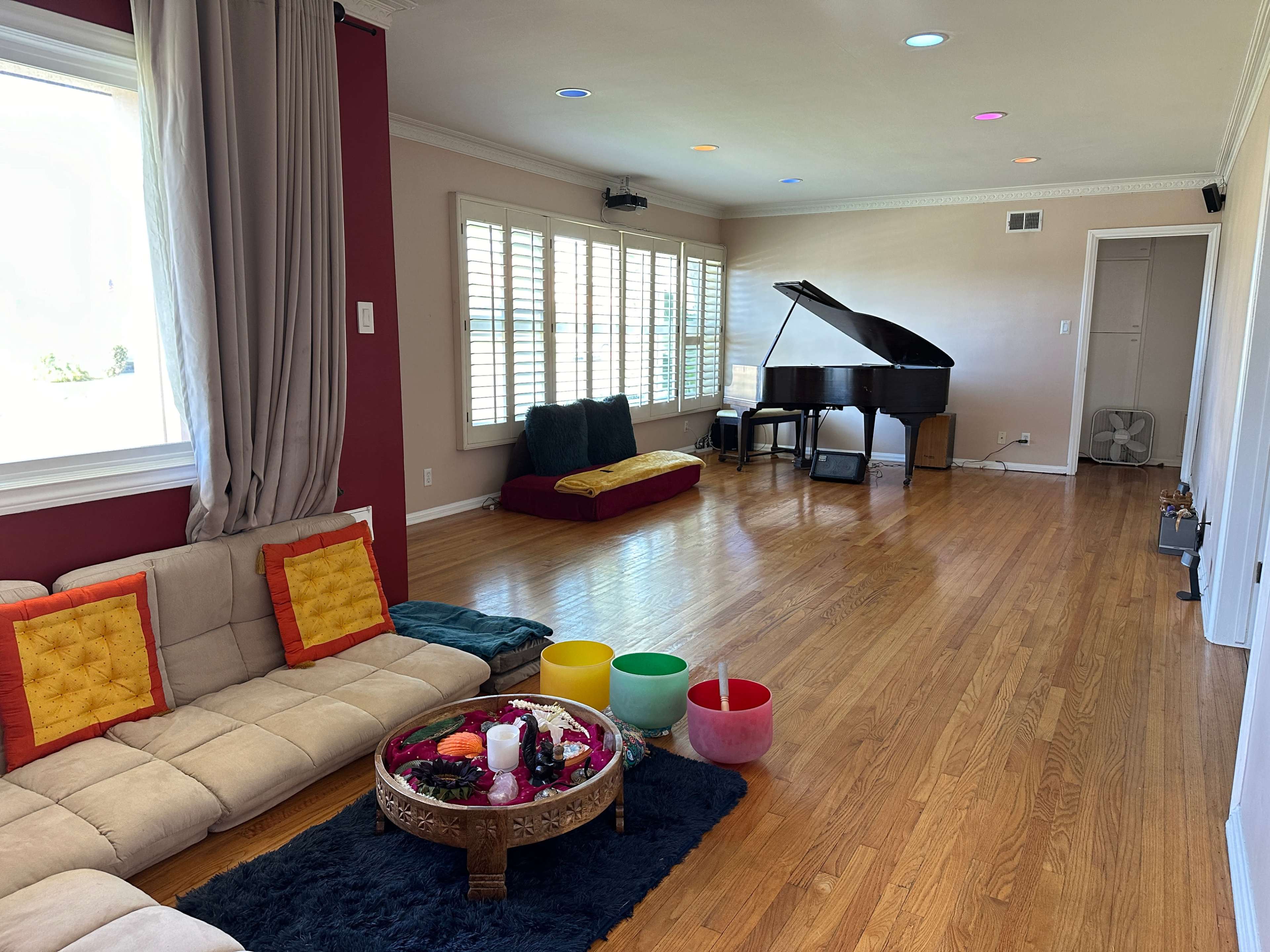 A spacious living room featuring a piano, a sectional sofa with decorative pillows, and a coffee table adorned with various colorful items.