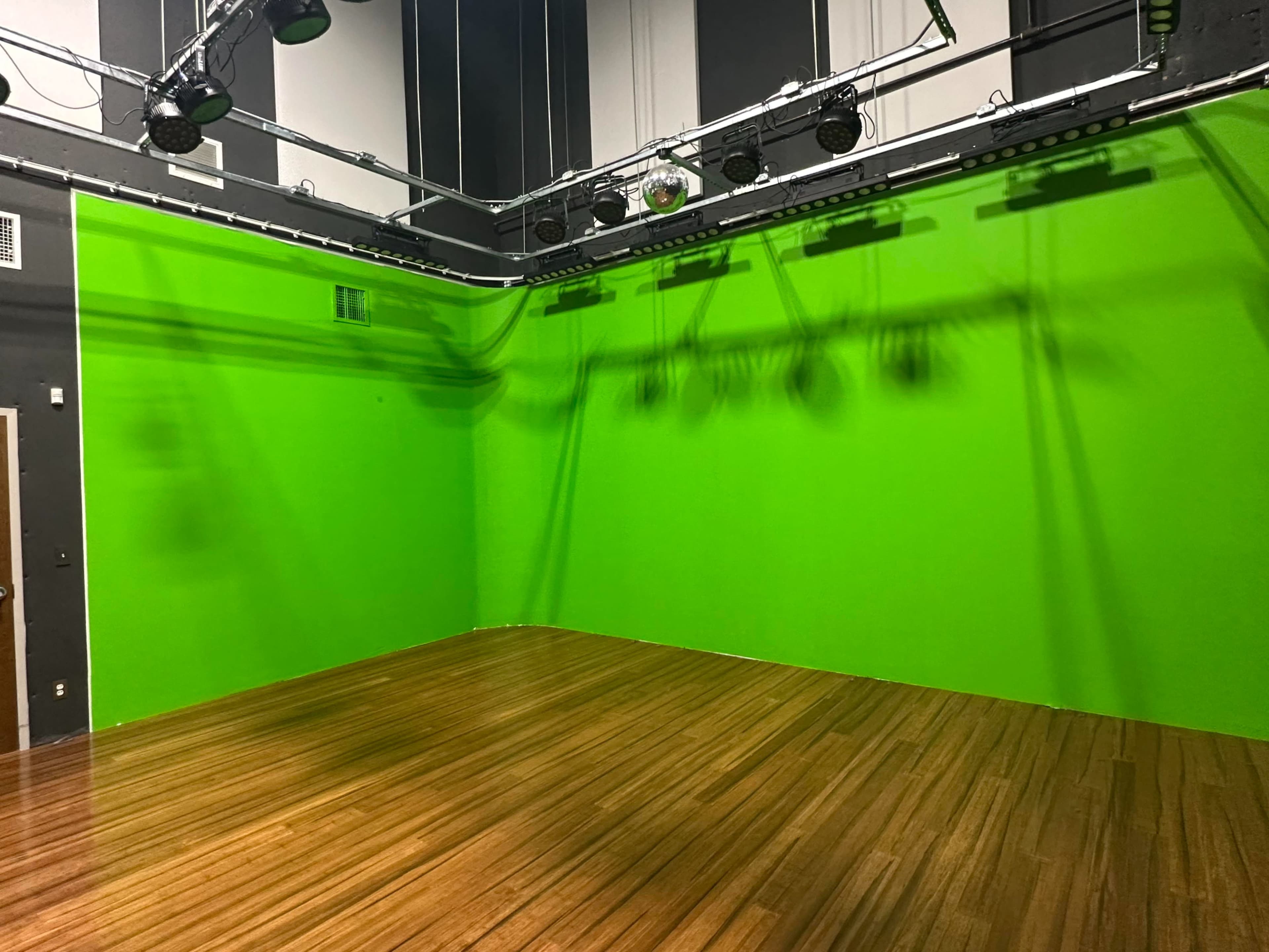 An empty studio space with a green screen wall and a polished wooden floor.