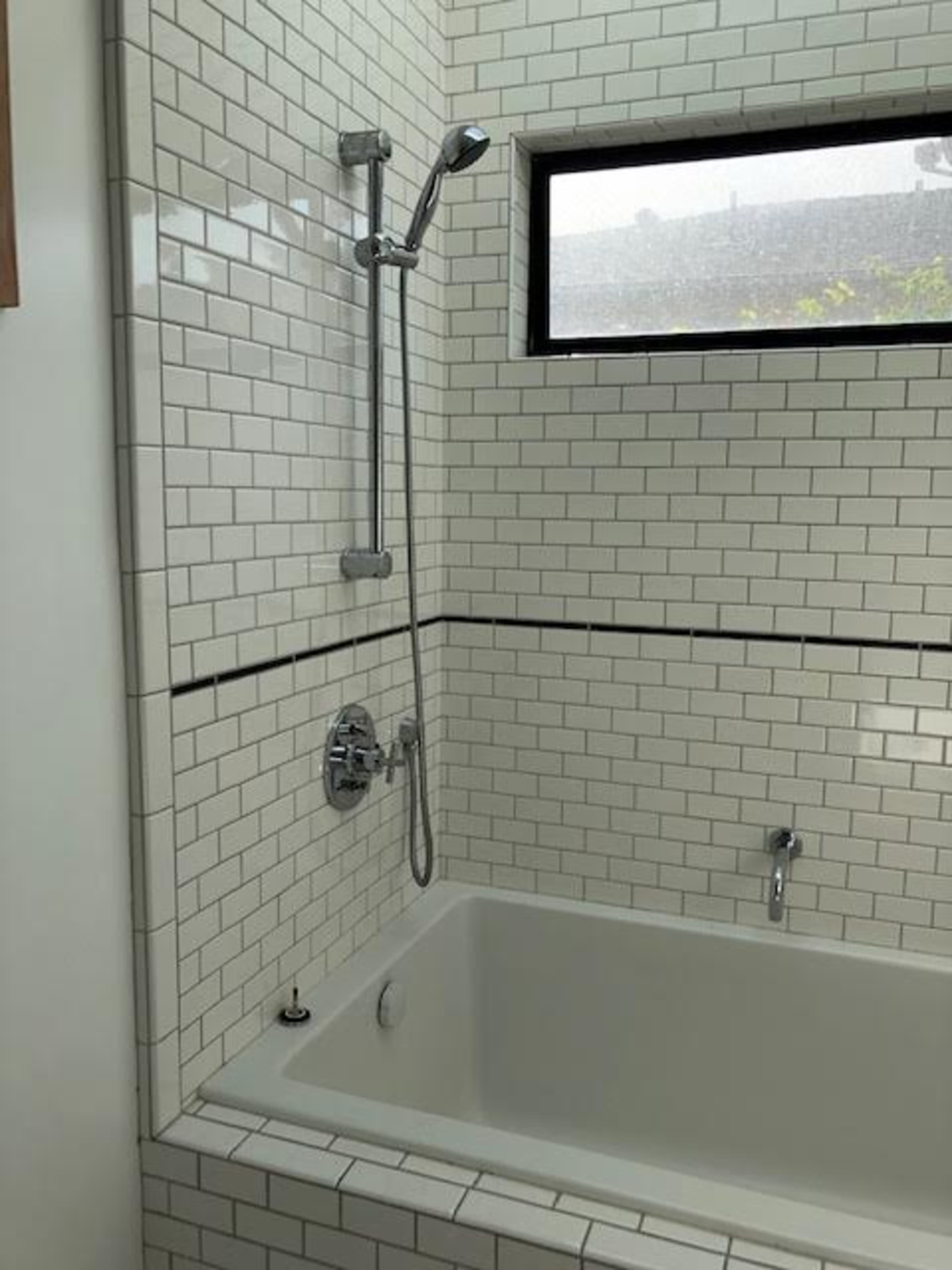 The image shows a modern bathroom featuring a shower and tub combo with white subway tile and a window above.