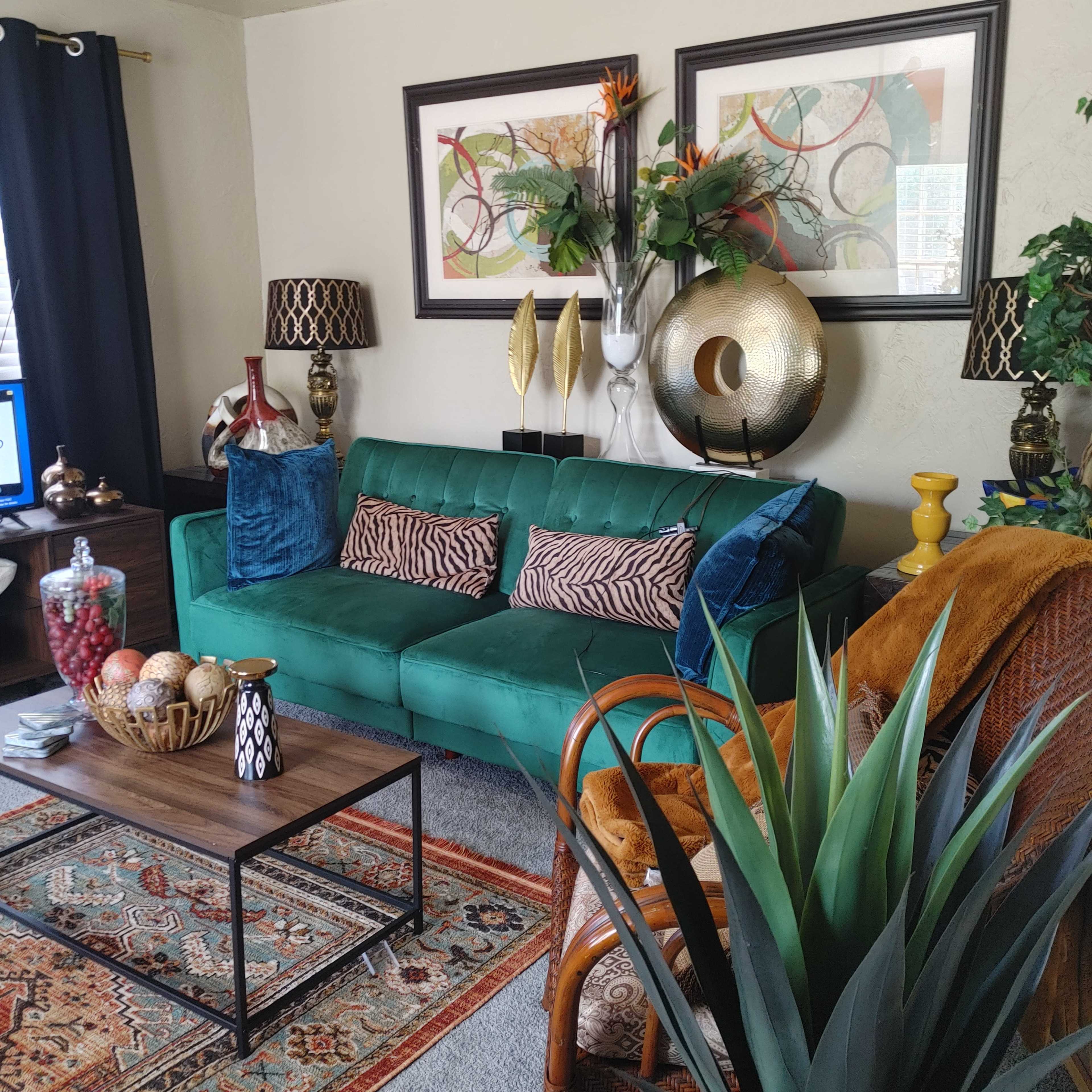The living room features a green velvet sofa, a wooden coffee table, and various decorative plants and art pieces on the walls.
