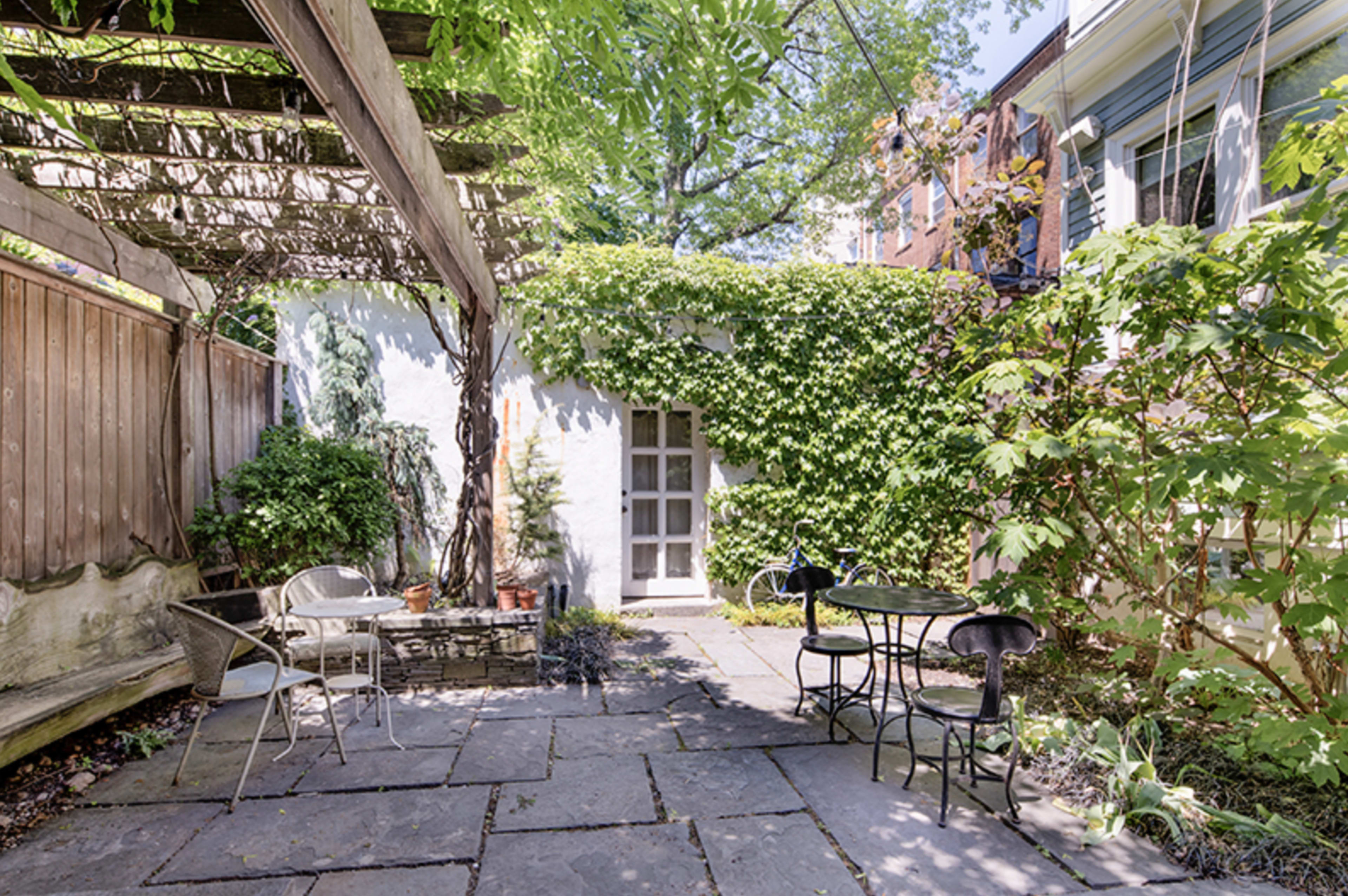 A stone patio surrounded by greenery, with a table and chairs set for outdoor seating.