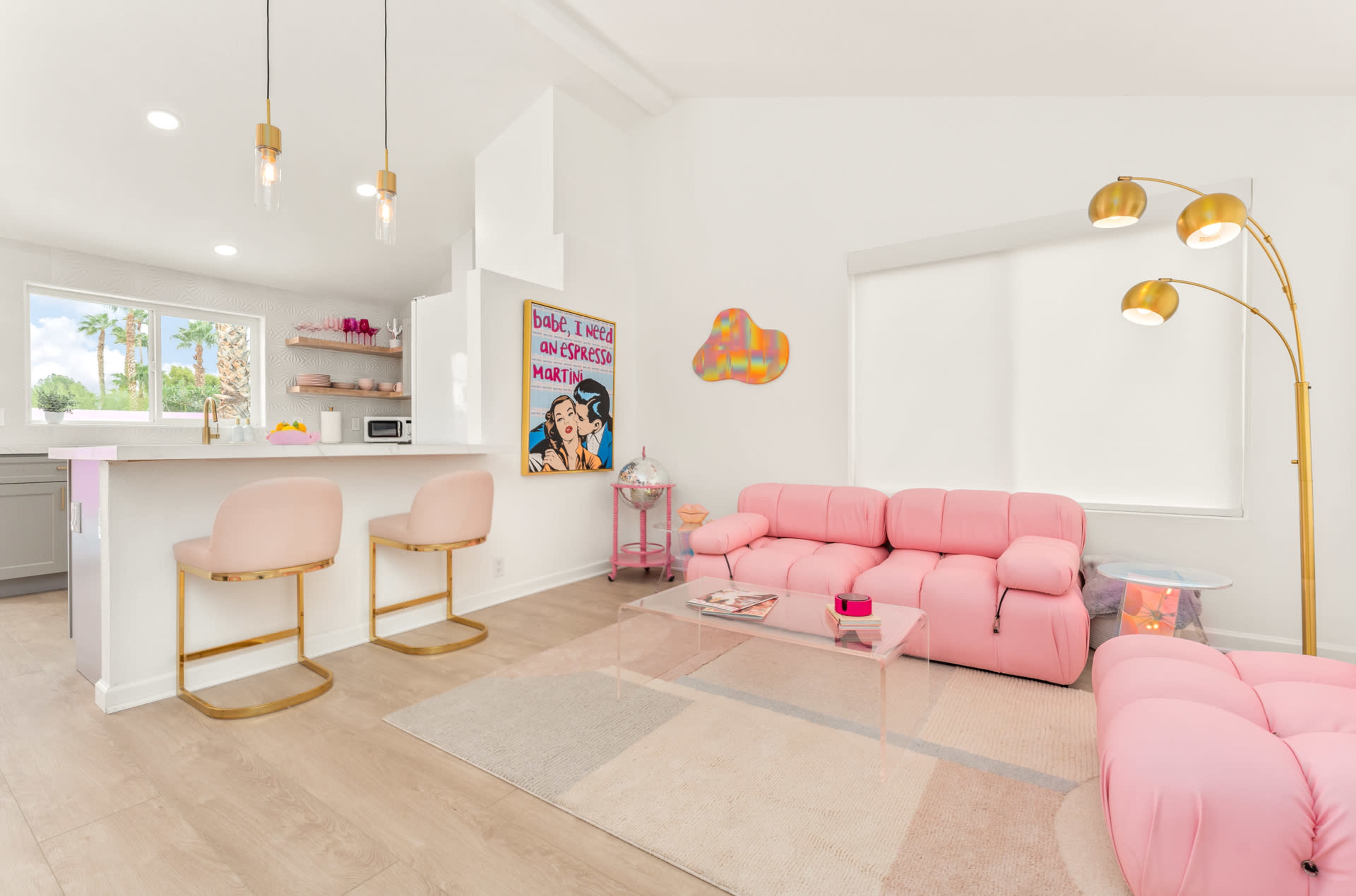 A bright living room features a pink sectional sofa, a glass coffee table, and a bar area with two stools.