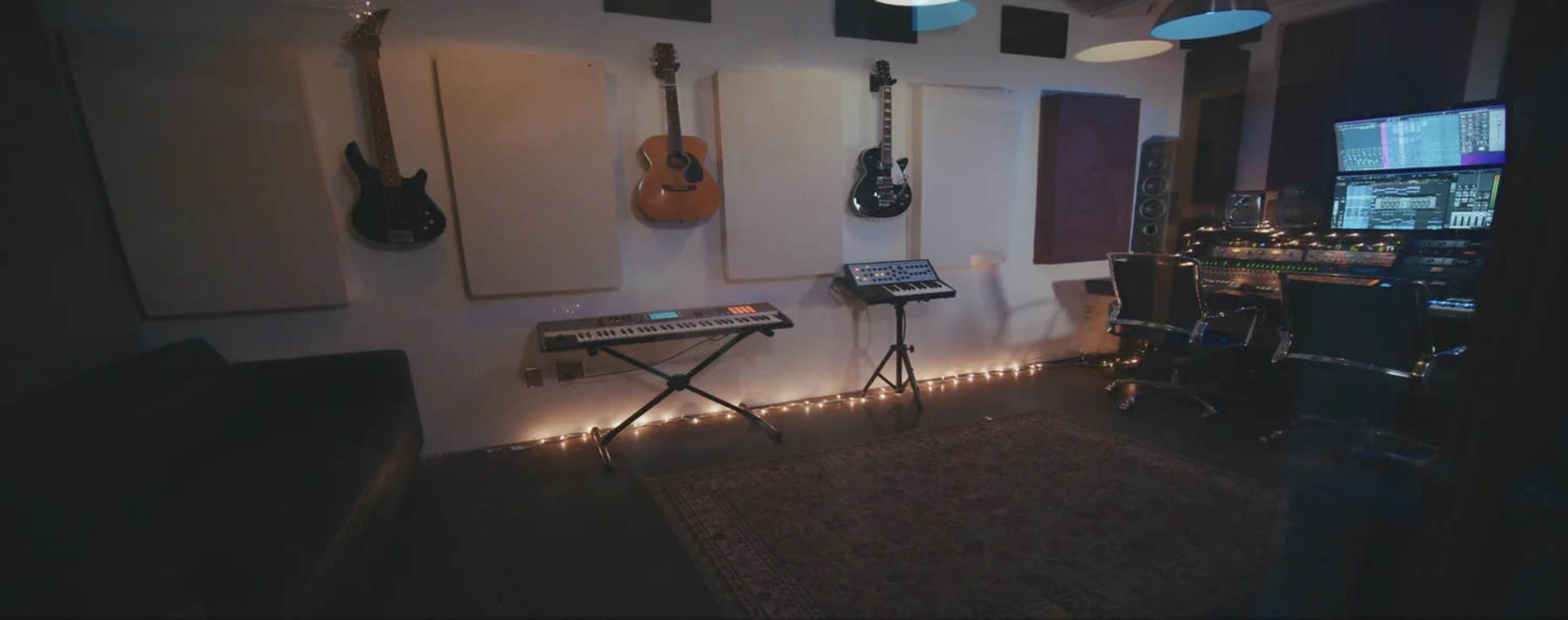 The image shows a music studio with various instruments, including guitars and a keyboard, along with sound equipment and a desk, illuminated by soft lighting.