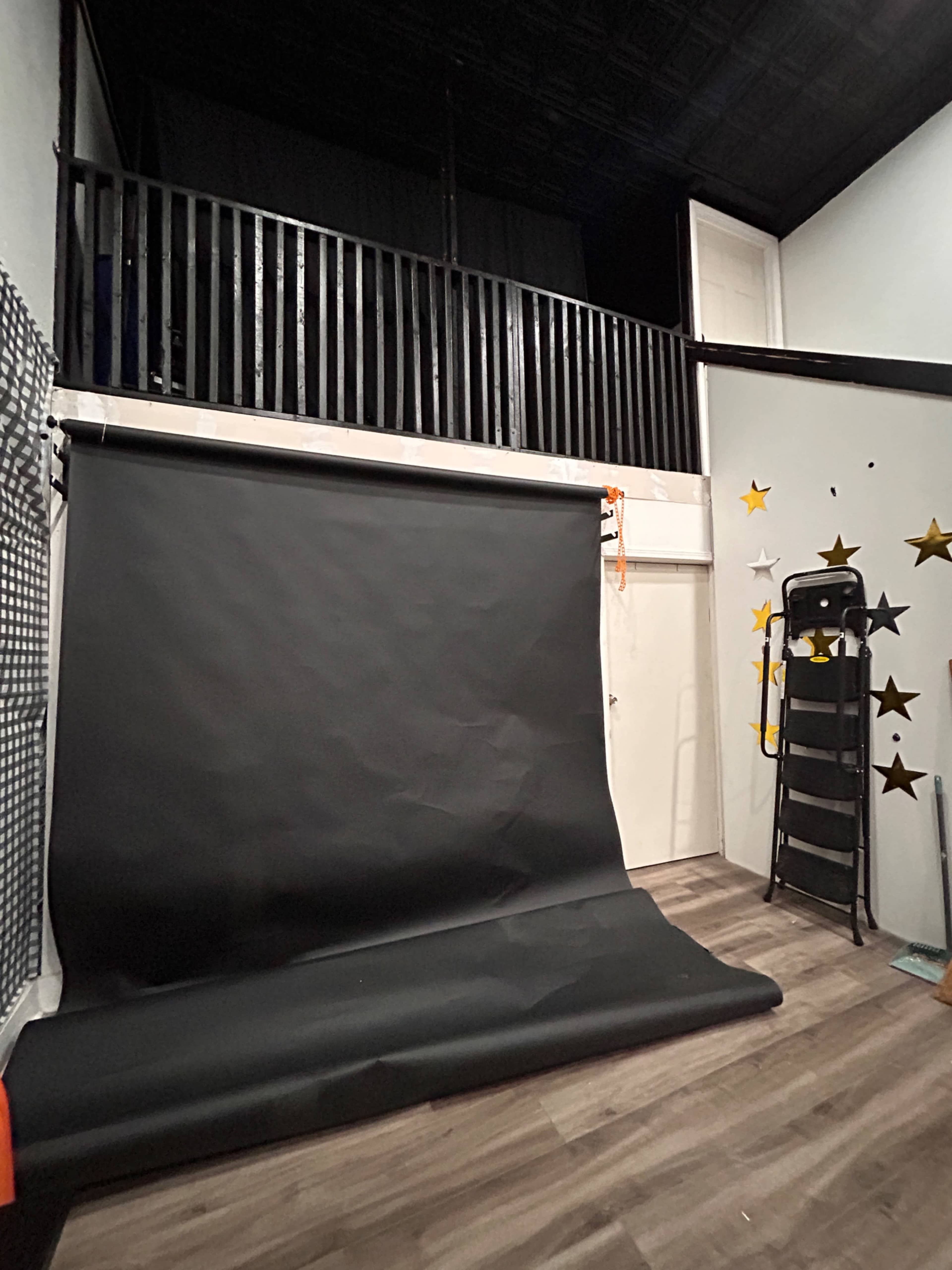 The image shows a photography studio with a black backdrop, a folding chair, and walls decorated with gold stars.