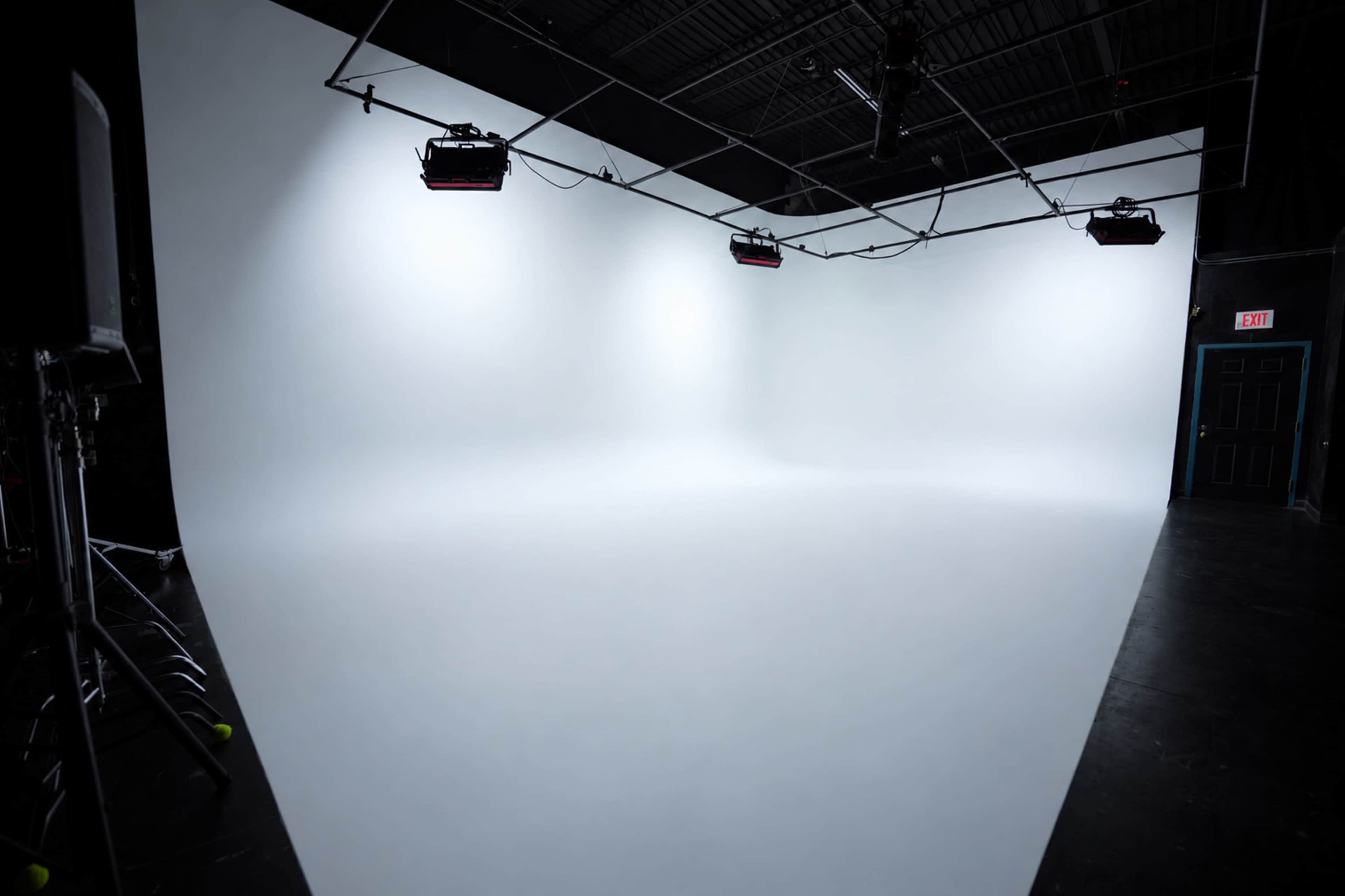 The image shows a spacious photography studio with a seamless white backdrop and overhead lighting equipment.