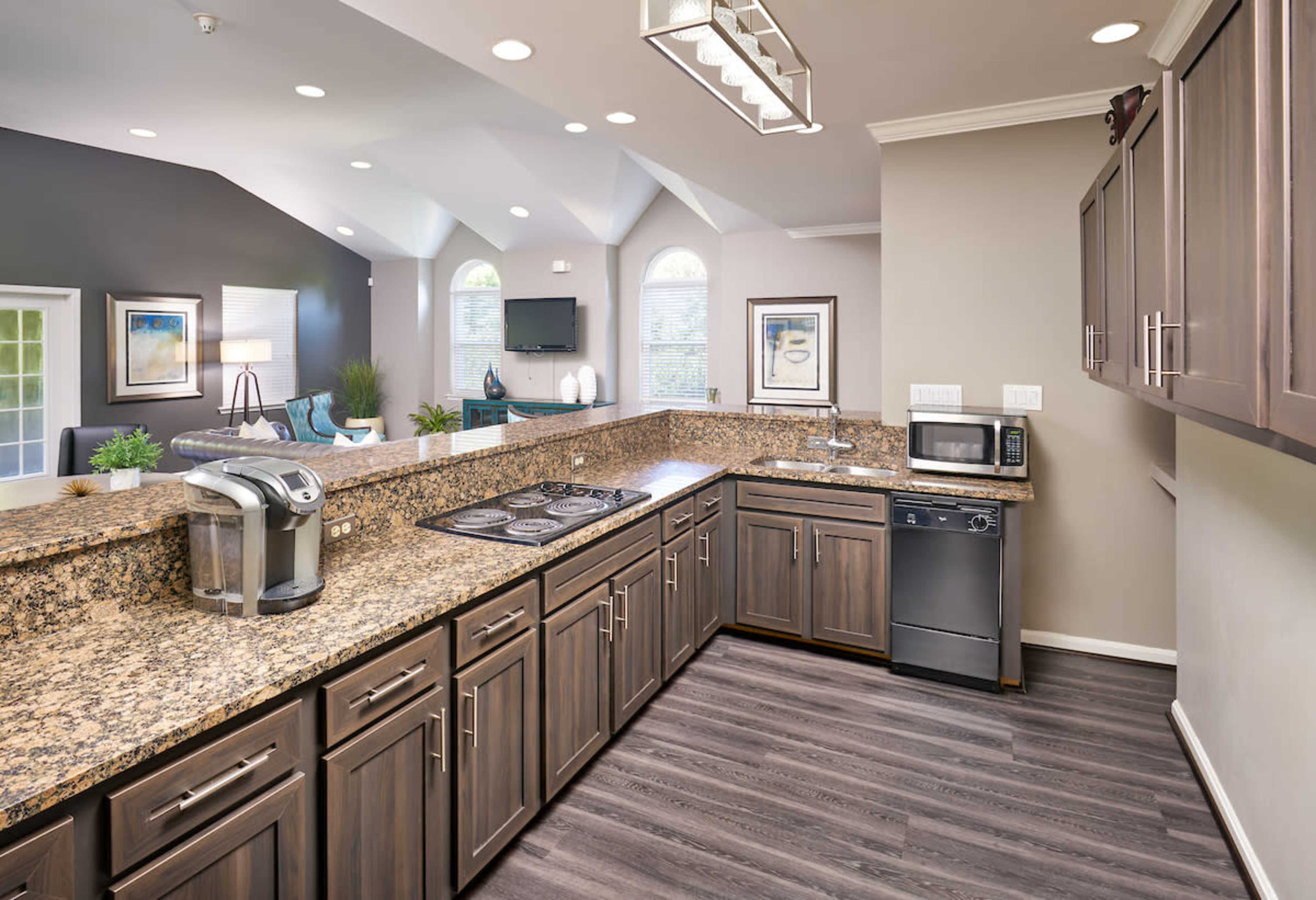 The image shows a modern kitchen featuring dark wood cabinets, a granite countertop, and built-in appliances like a microwave and a coffee maker.