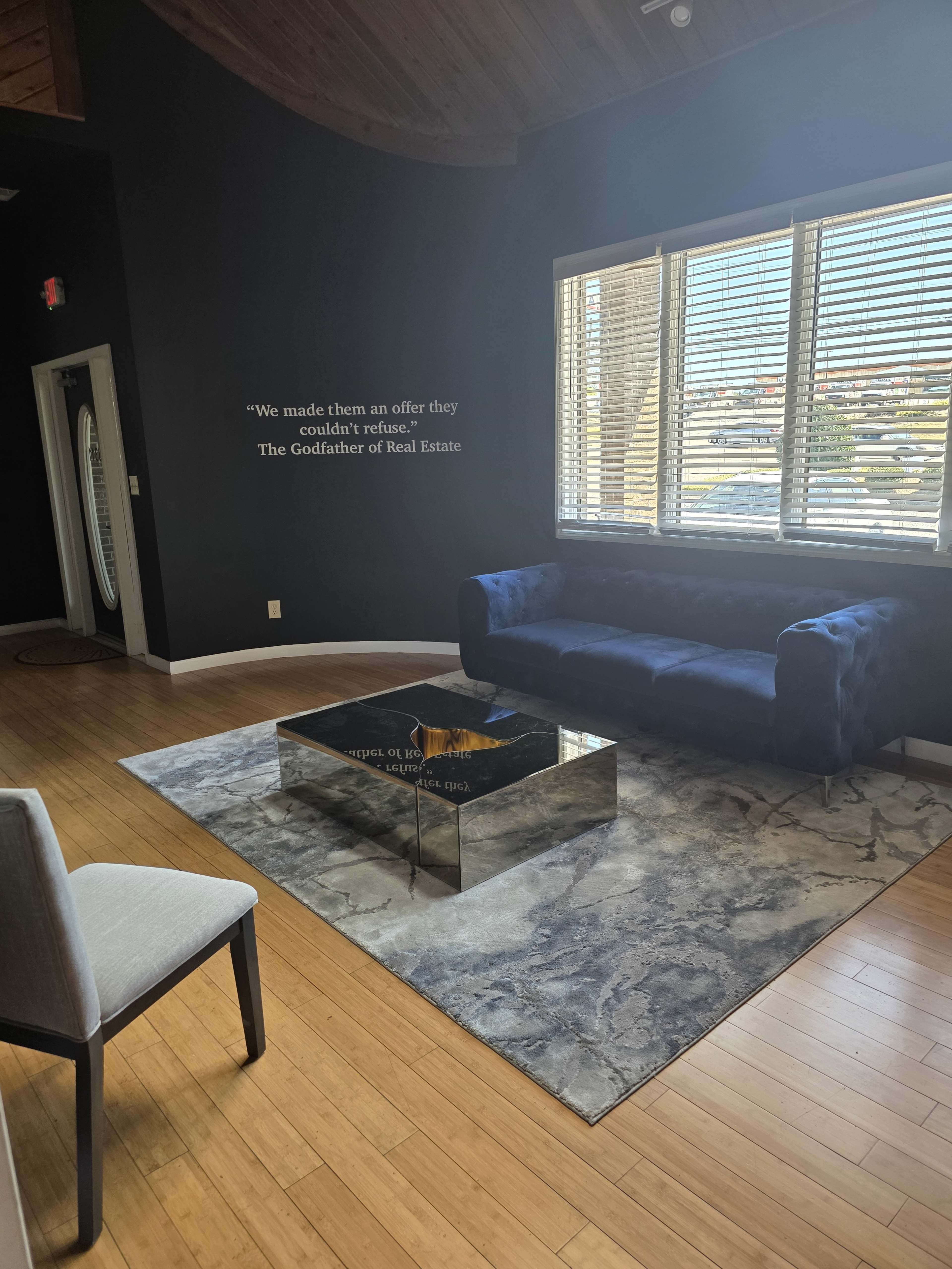 The image shows a modern, spacious room with a blue velvet sofa, a glass coffee table, and large windows.