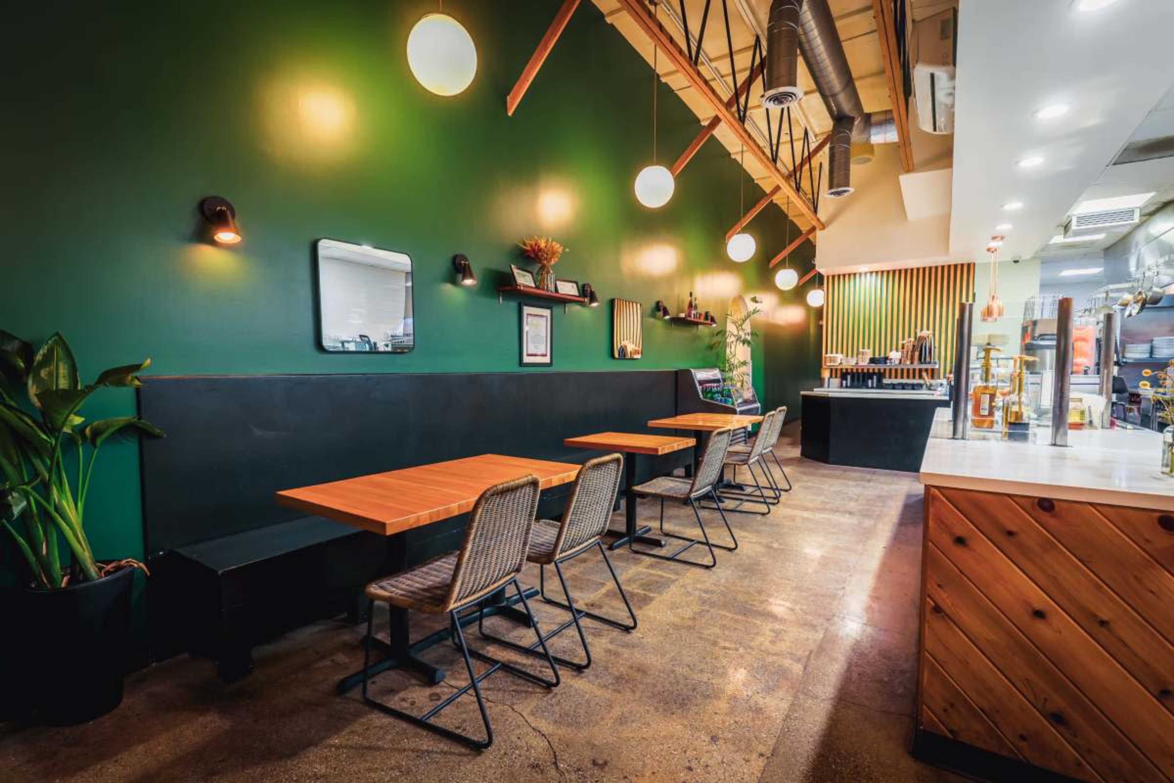 The image shows a modern café interior featuring wooden tables and chairs, green walls, and pendant lighting.
