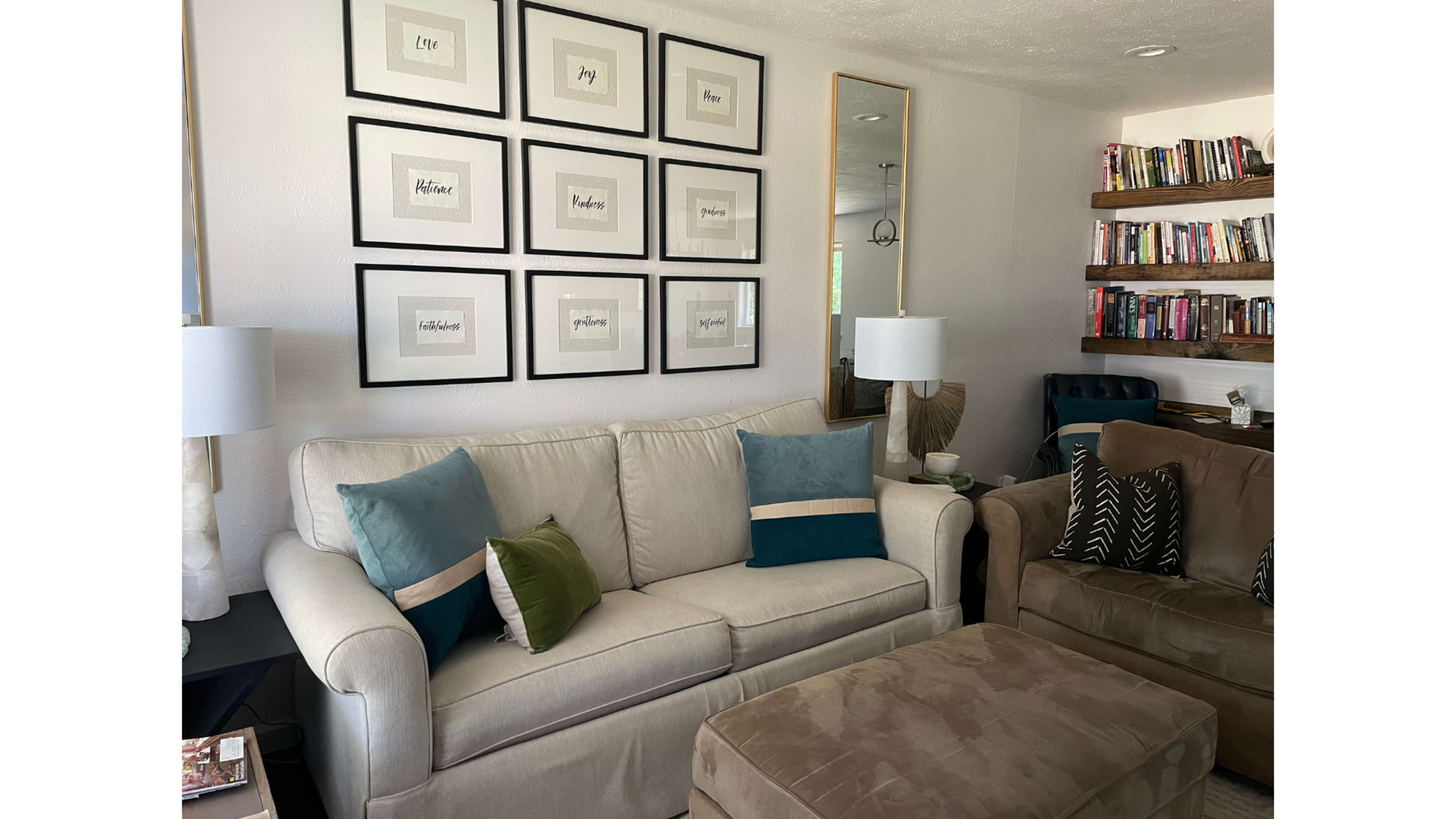 A living room with a beige sofa, a brown armchair, a decorative wall of framed art, and a bookshelf filled with books.