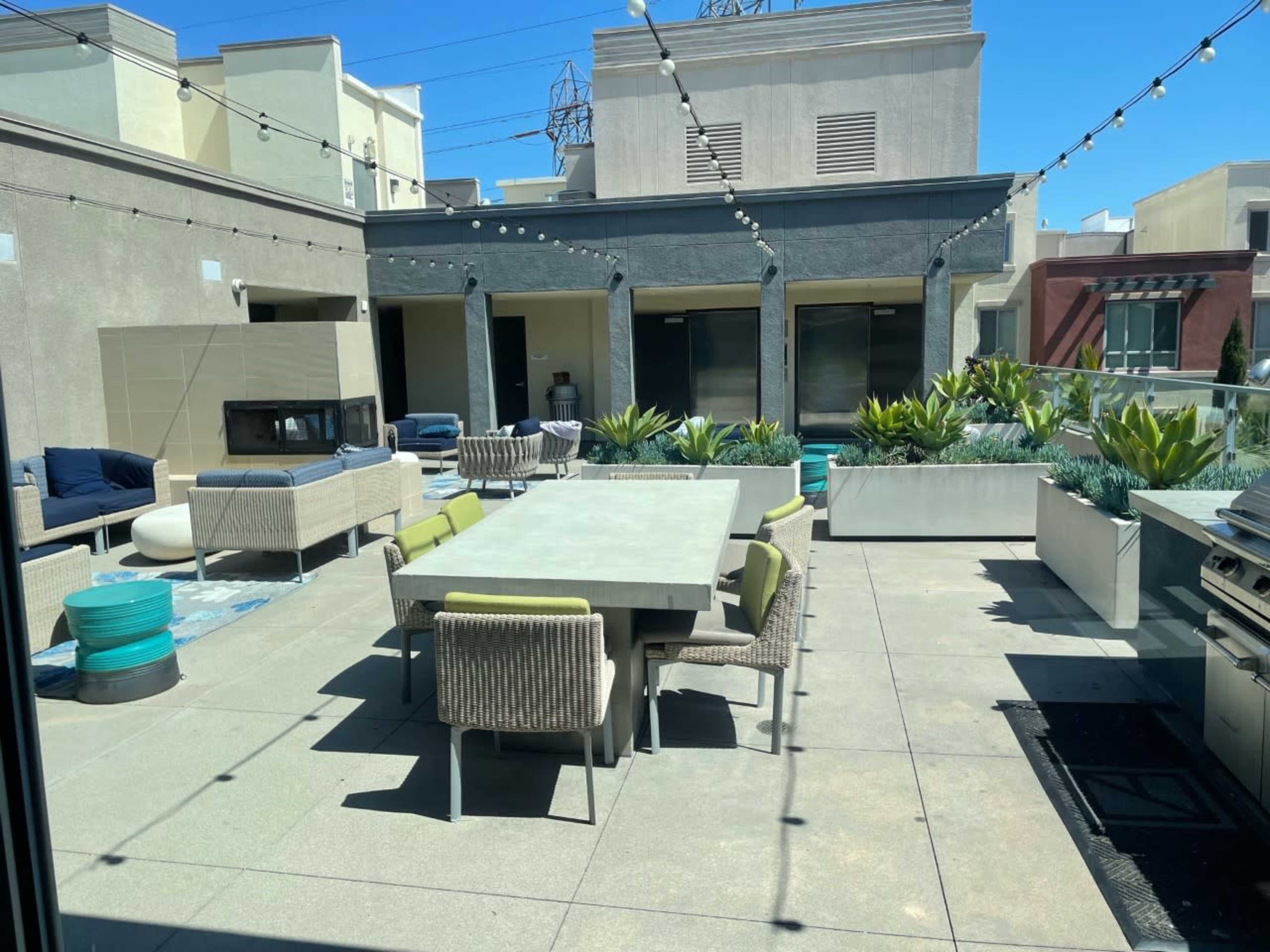 A modern rooftop terrace featuring a large dining table surrounded by various seating areas and planters.