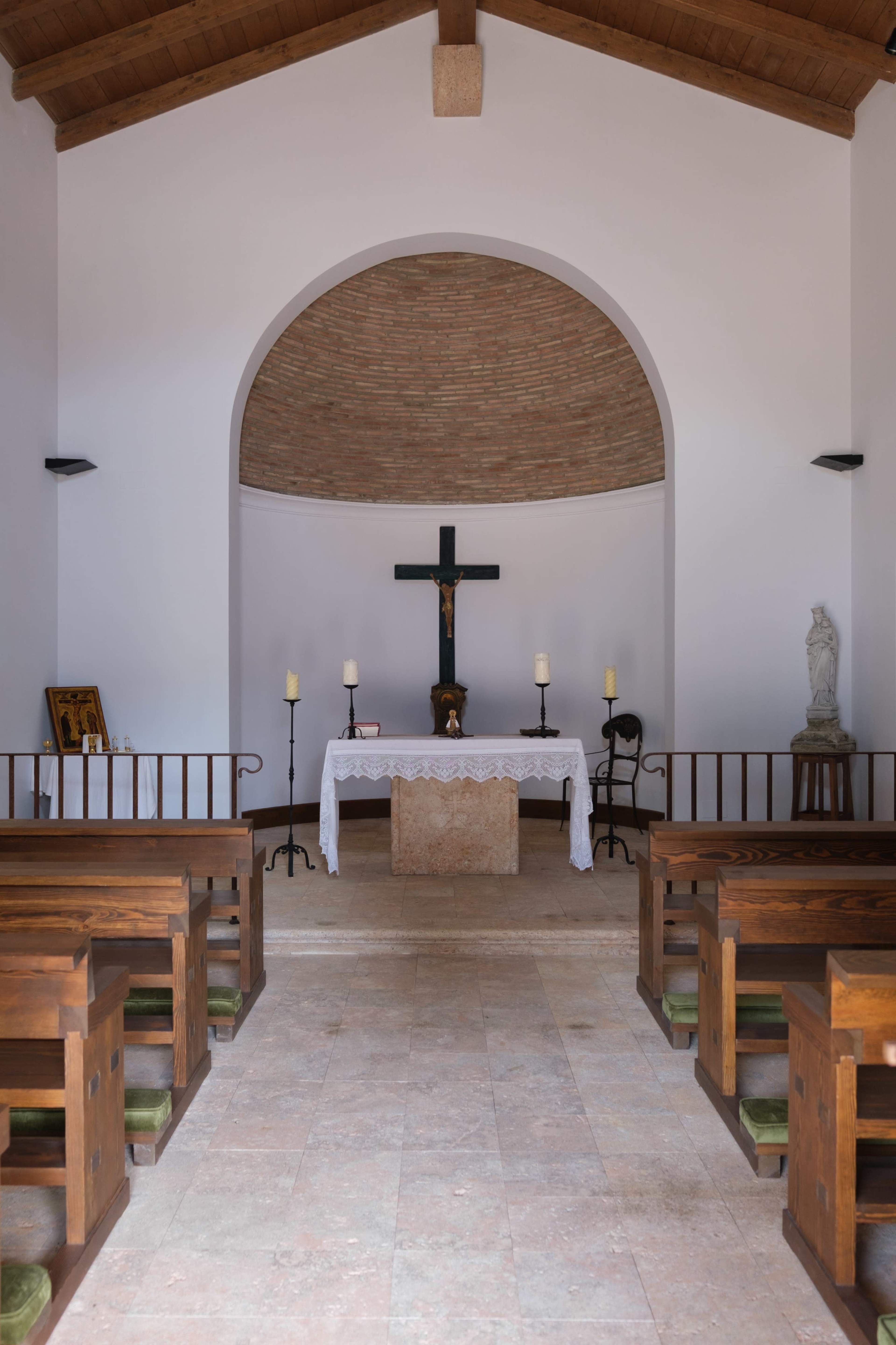The image shows the interior of a small church featuring a wooden altar with a cross, surrounded by benches for worshippers.